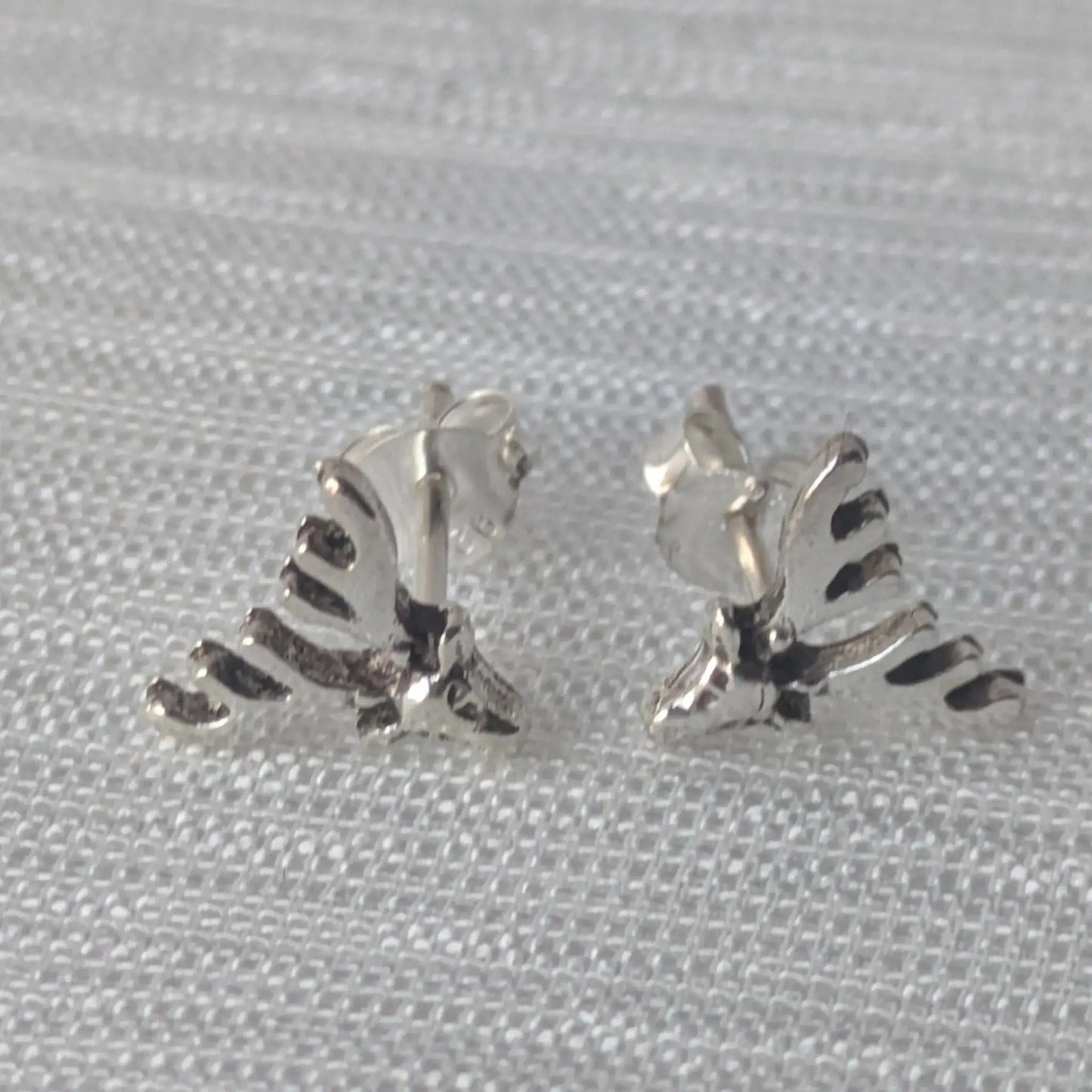 Zwei detaillierte Elch-Geweih-Ohrstecker aus glänzendem 925 Sterling Silber, liegend auf einem hellen, strukturierten Stoff.