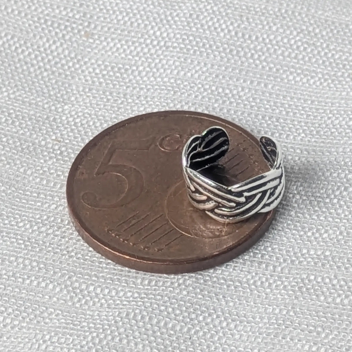 Größenvergleich der silbernen Flechtmuster-Ohrklemme, die flach auf einer 5-Cent-Münze liegt.