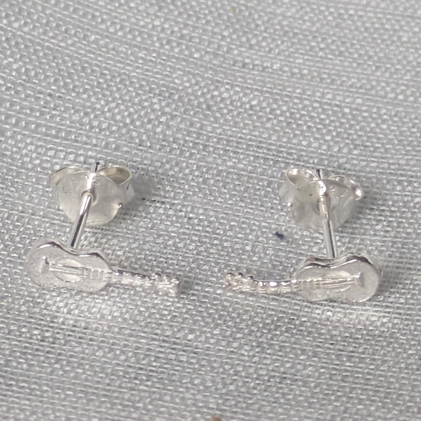 Paar silberne Gitarren Ohrstecker als dezenter Musikschmuck für Damen und Herren, präsentiert auf neutralem Hintergrund.