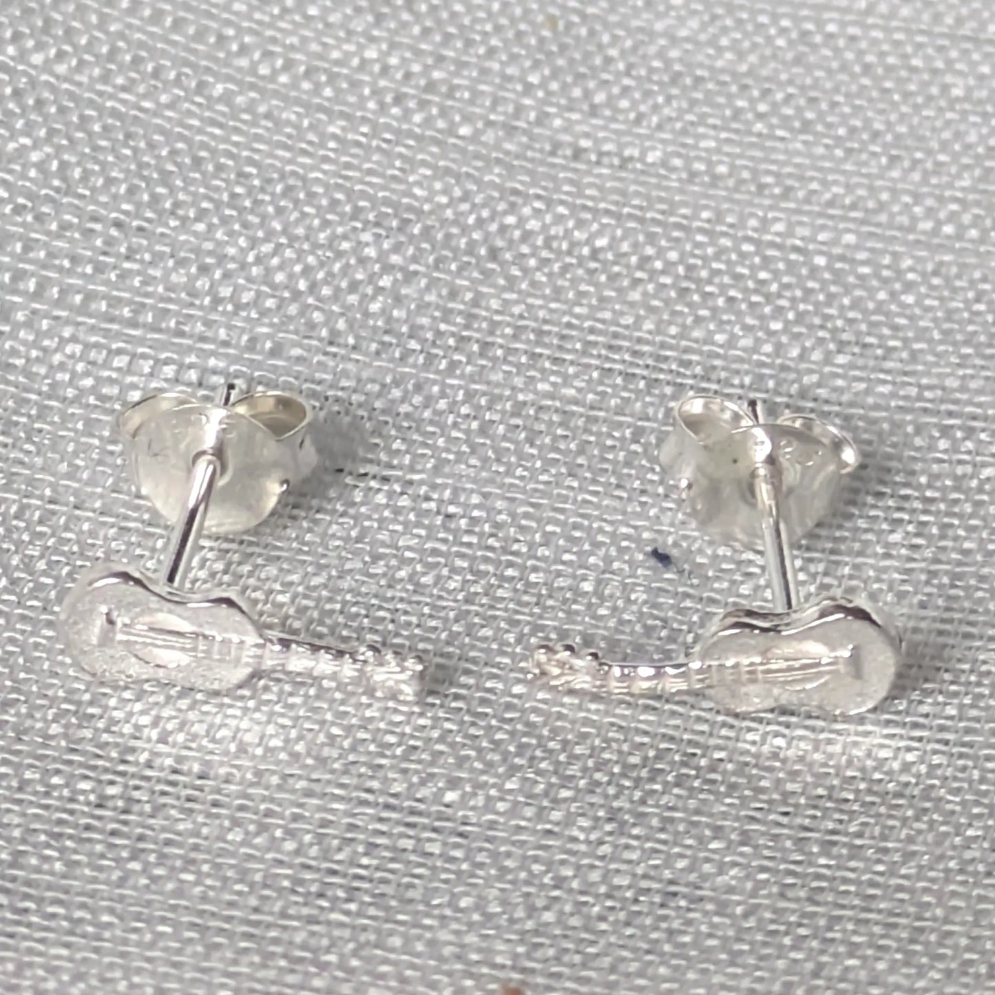 Paar silberne Gitarren Ohrstecker als dezenter Musikschmuck für Damen und Herren, präsentiert auf neutralem Hintergrund.