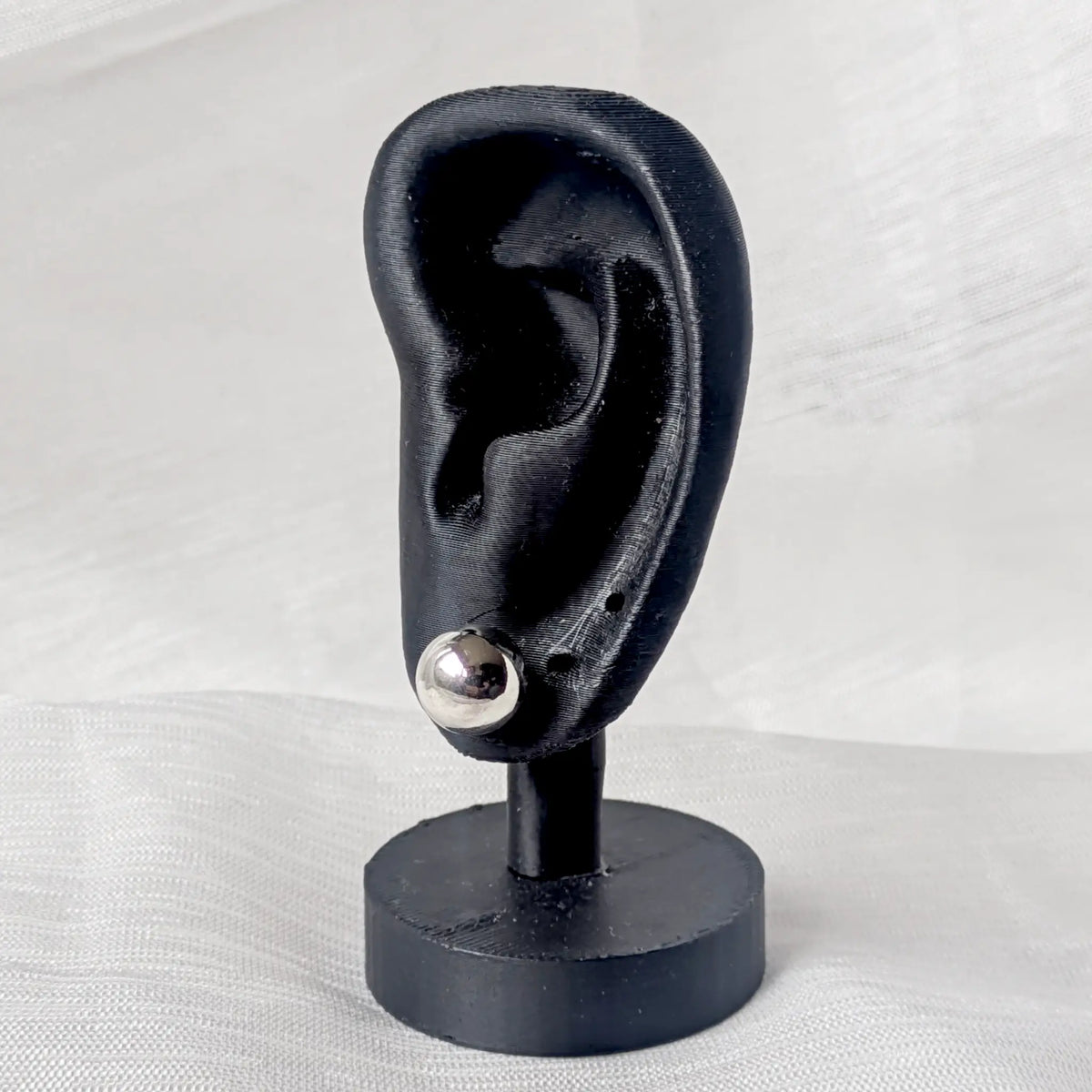 Ein 10mm großer Silber-Kugelohrstecker, dezent und elegant an einem schwarzen 3D-Ohr-Display präsentiert.