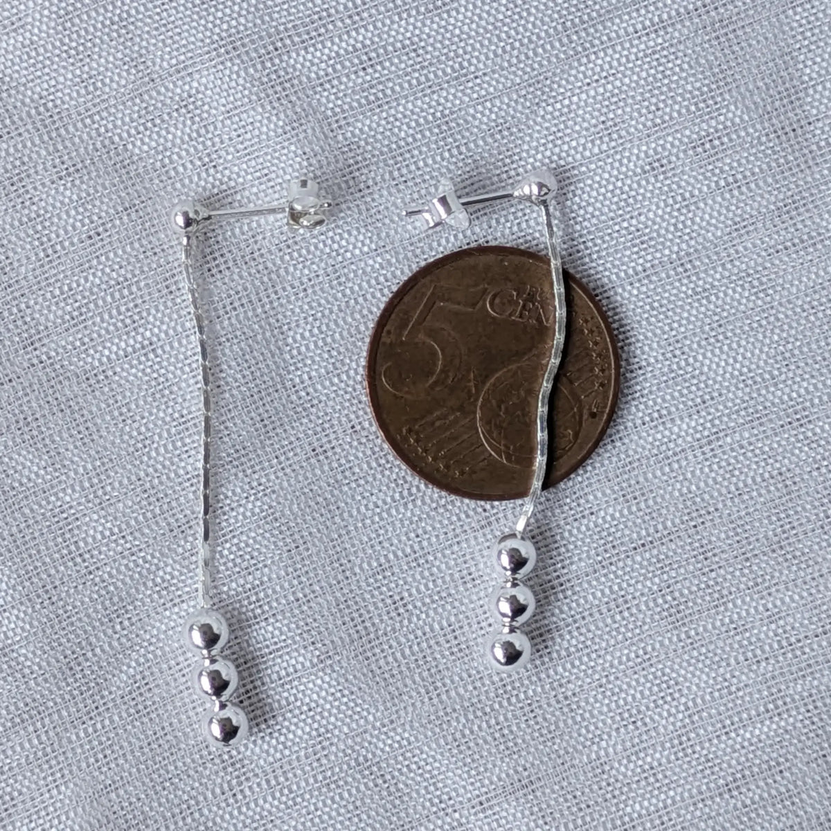Größenvergleich der langen, zierlichen Kugel-Silberohrringe liegend neben einer 5-Cent-Münze zur exakten Verdeutlichung der filigranen Proportionen.