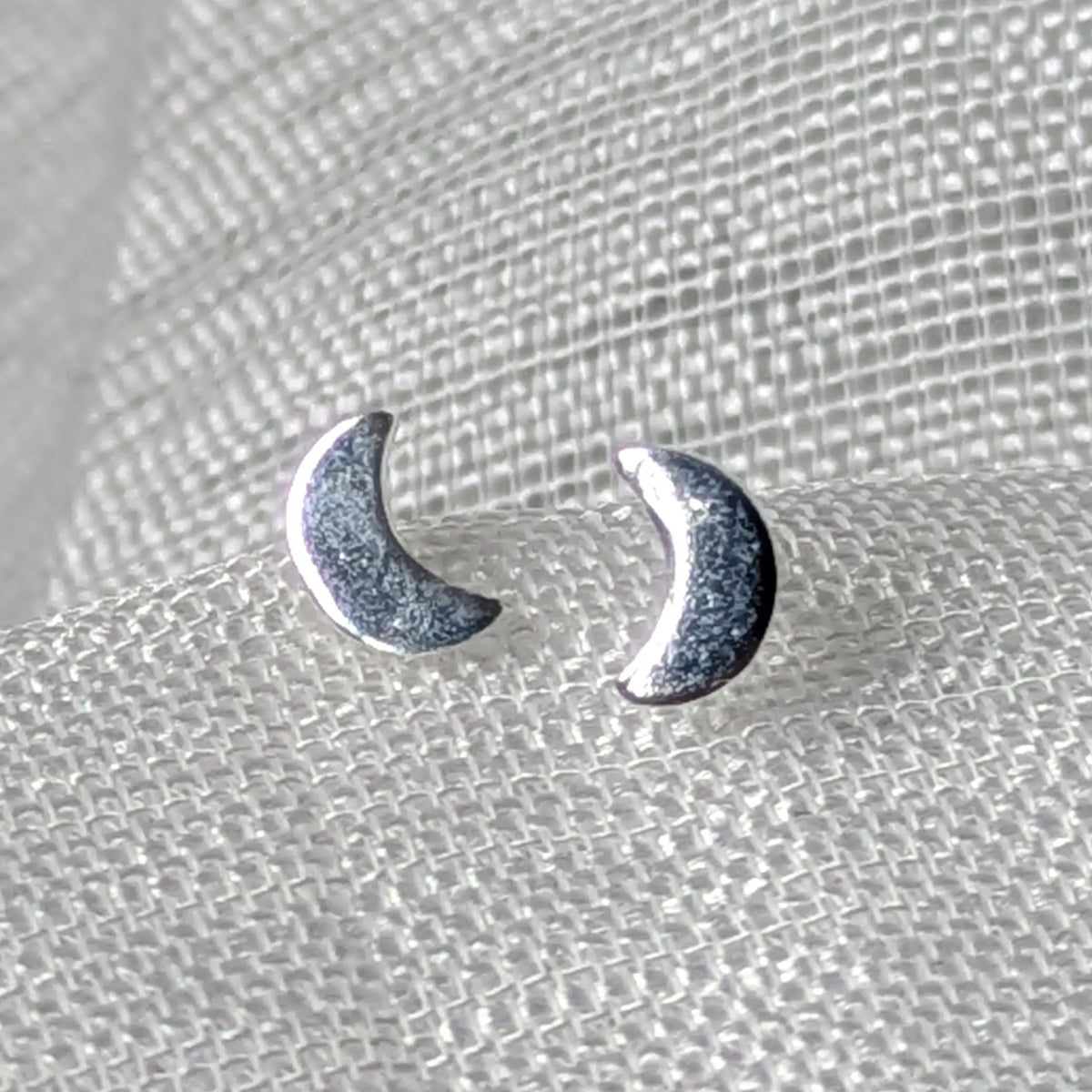 Frontalansicht der kleinen silbernen Mond-Ohrringe mit polierter, geschwungener Oberfläche.