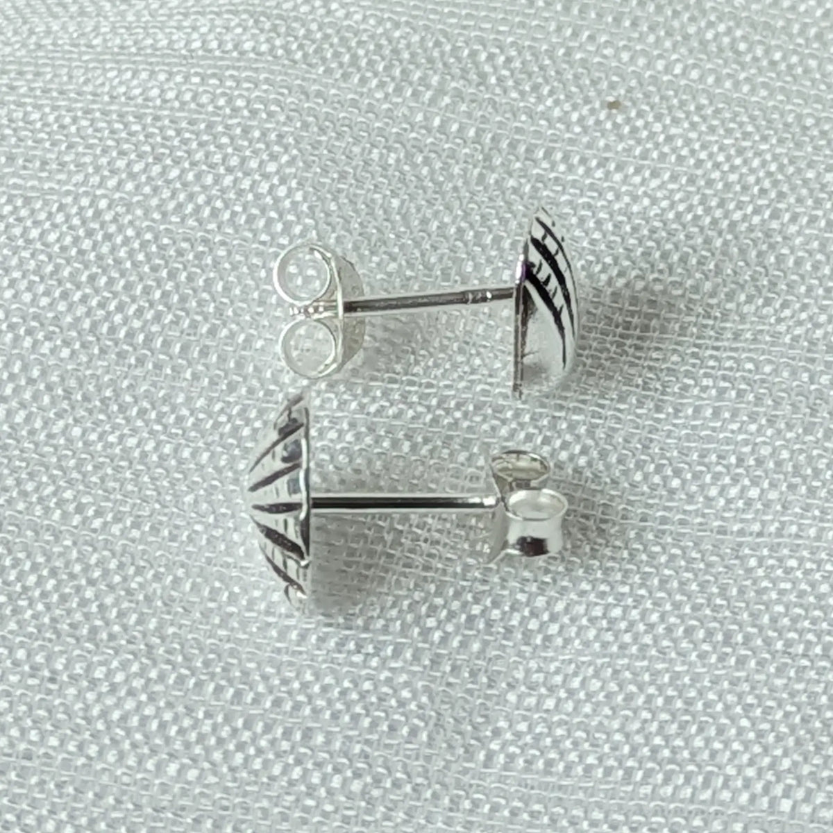 Seitenansicht der flachen Muschel-Ohrstecker aus Silber, die das anliegende Profil am Ohr verdeutlicht.