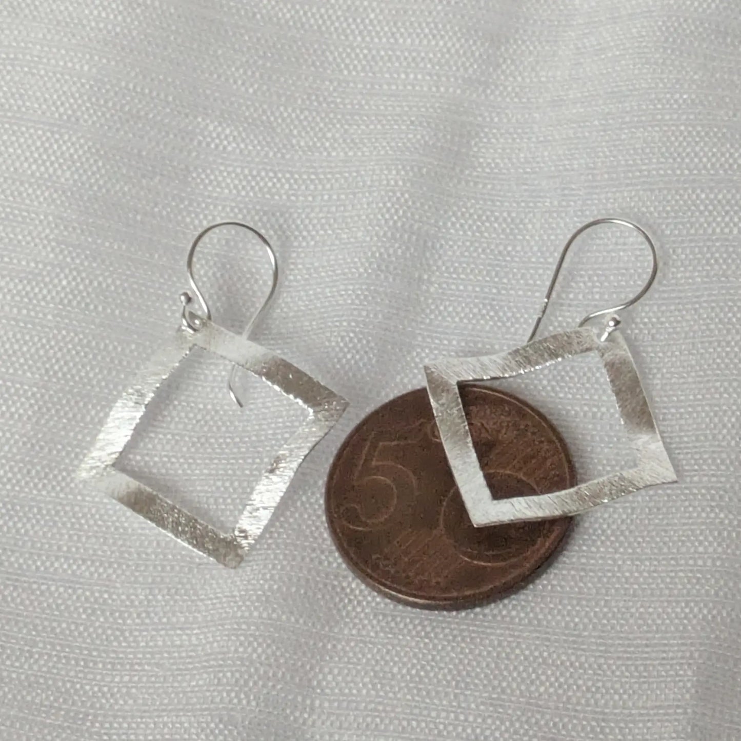 Größenvergleich der großen geometrischen Silber-Ohrhänger neben einer 5-Cent-Münze.
