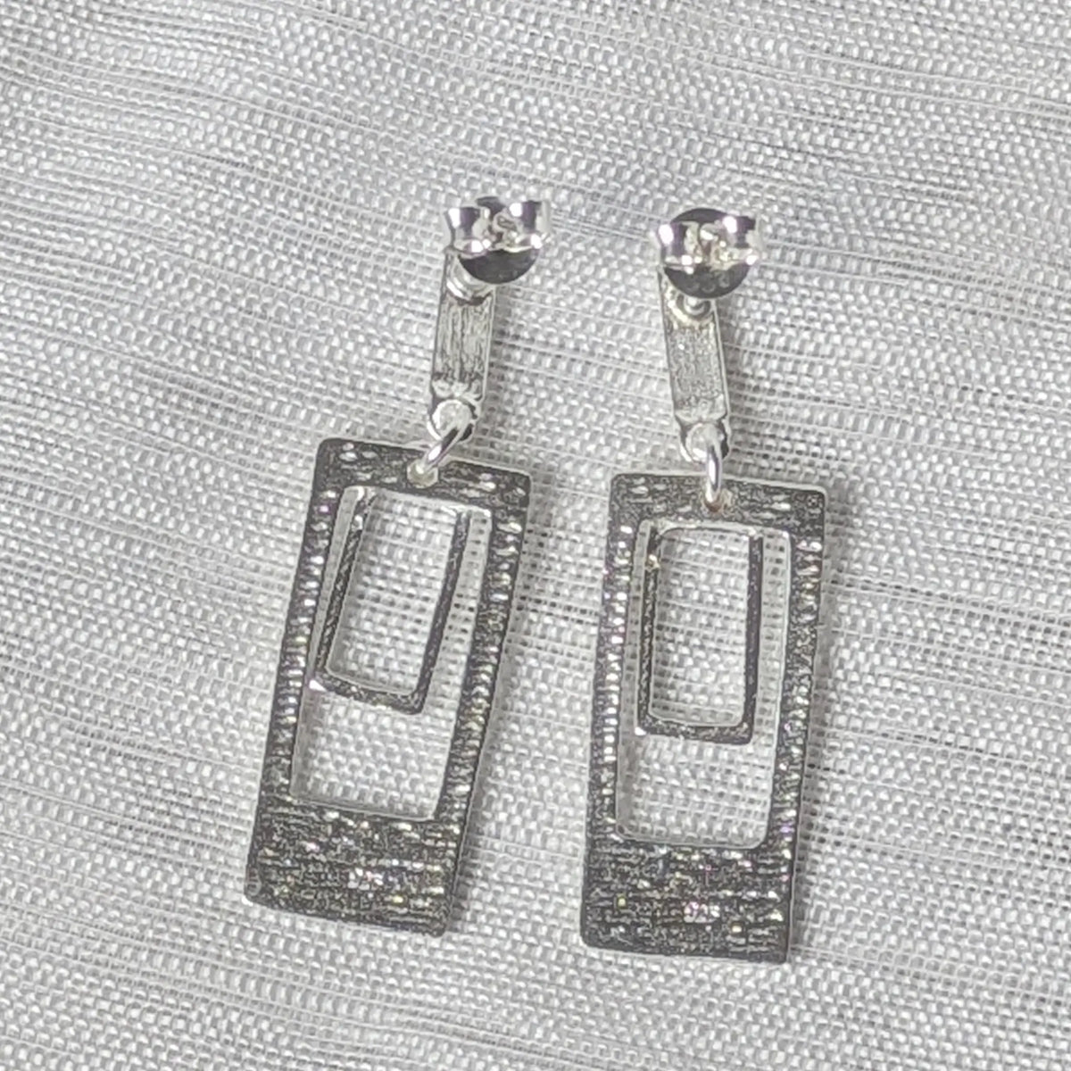 Rückansicht der geometrischen 925 Silber Ohrstecker, Fokus auf die strukturierte Oberfläche und die bewegliche Aufhängung.