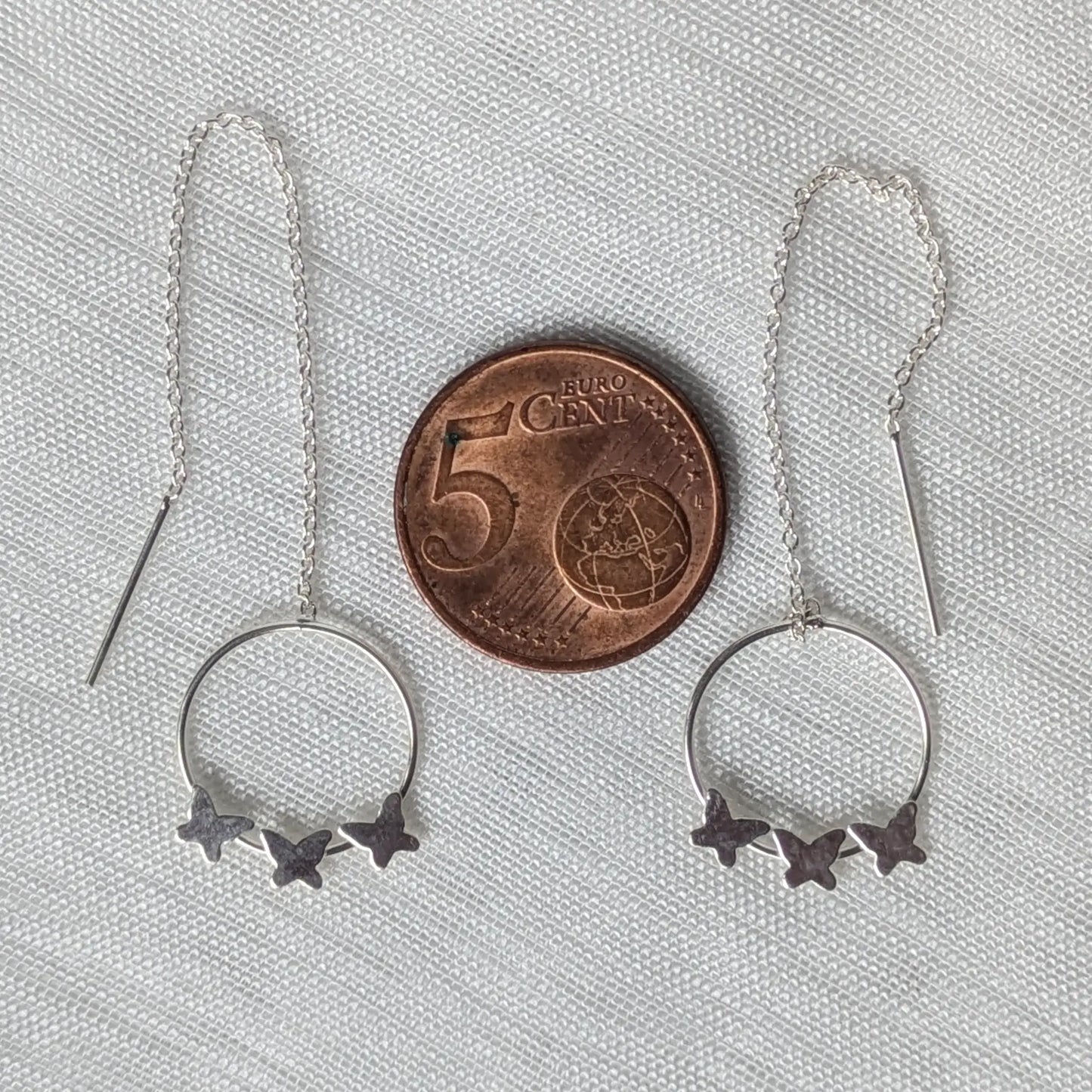 Größenvergleich des runden Schmetterlings-Elements der Silberohrringe direkt neben einer 5-Cent-Münze.