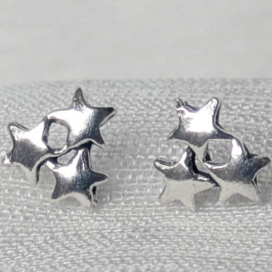 Detaillierte Nahaufnahme von zwei glänzenden Dreifach-Stern-Ohrsteckern aus 925 Sterling Silber auf einer hellen Gewebestruktur
