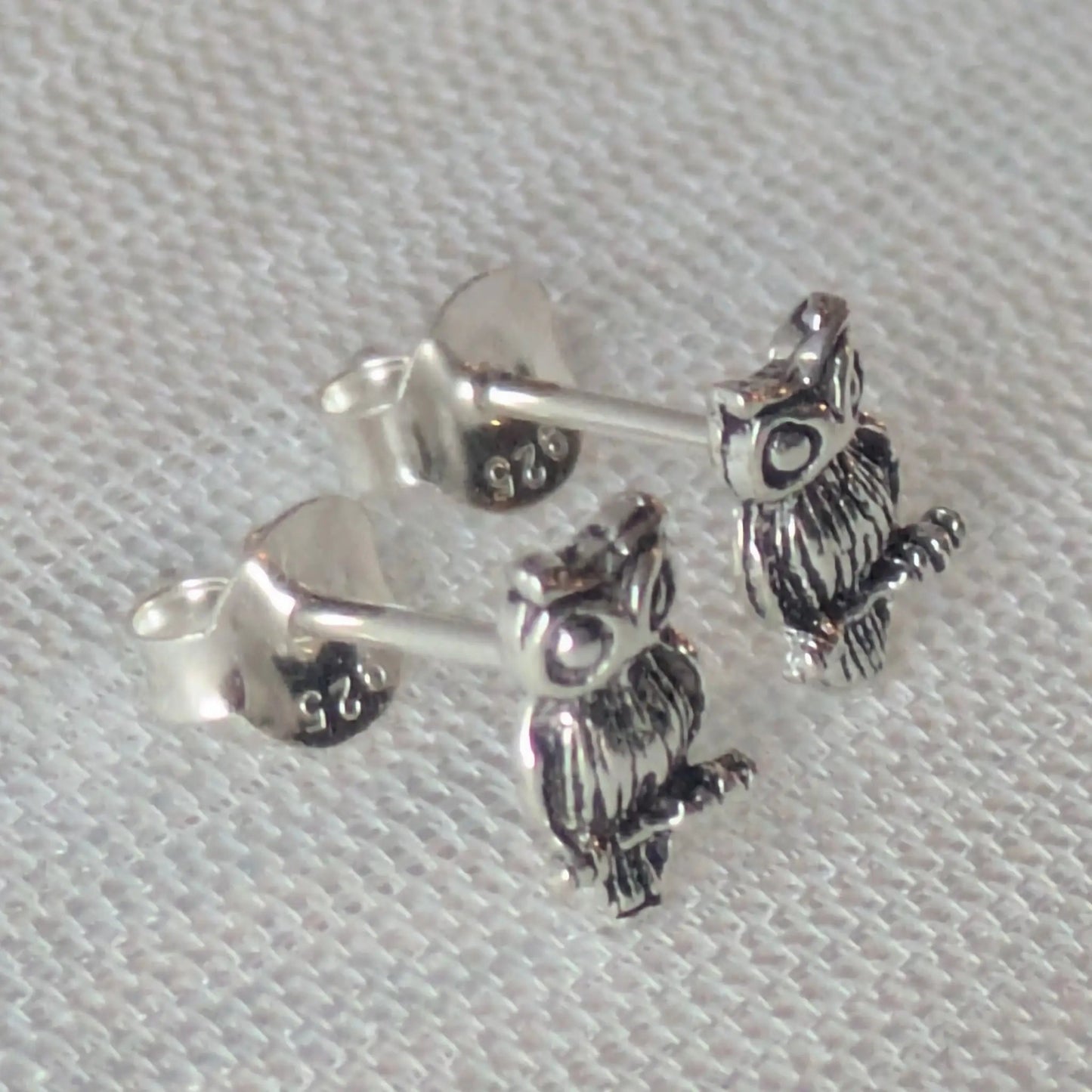 Paar detaillierte Eulen-Ohrstecker aus 925 Sterling Silber auf weißem Stoff fotografiert.