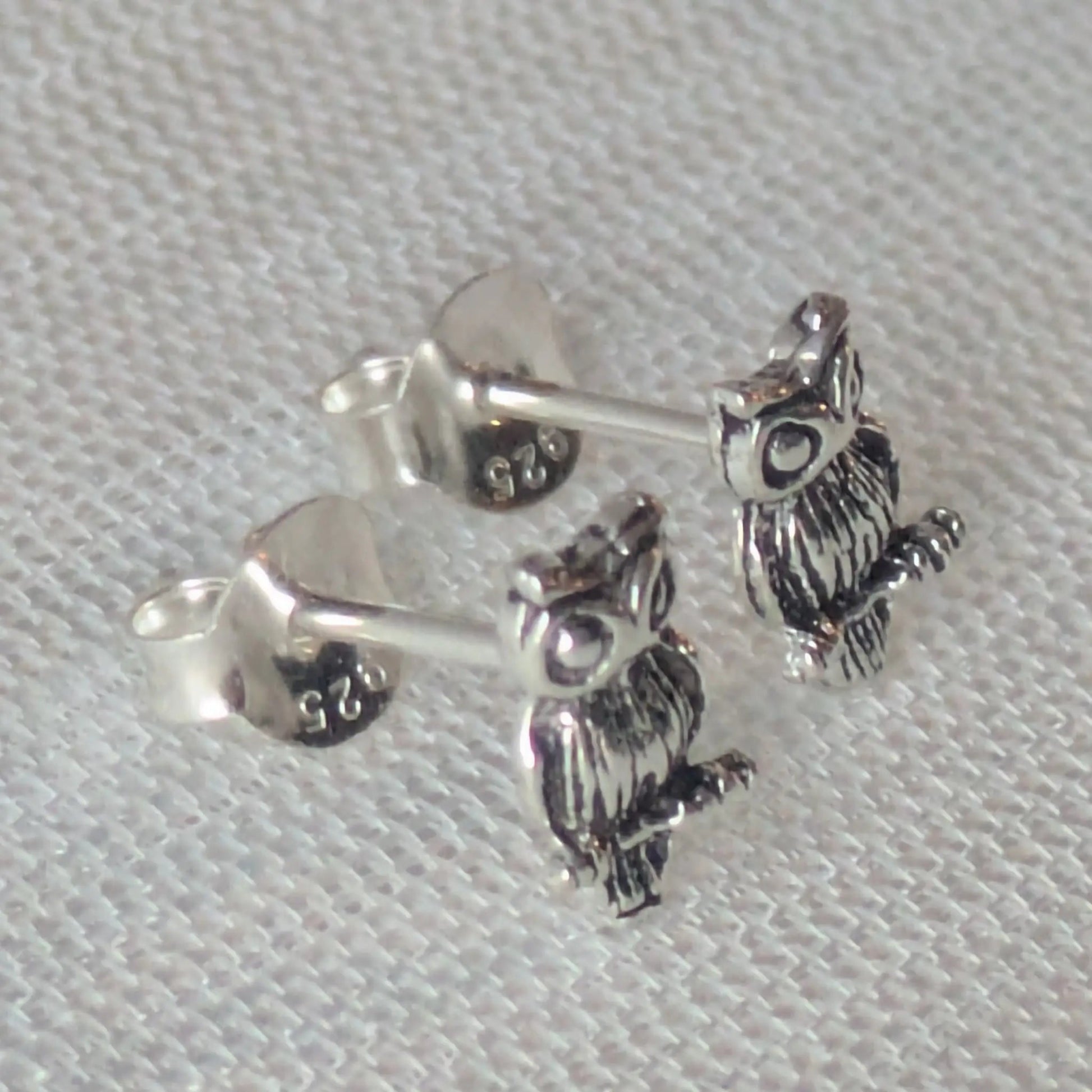 Paar detaillierte Eulen-Ohrstecker aus 925 Sterling Silber auf weißem Stoff fotografiert.