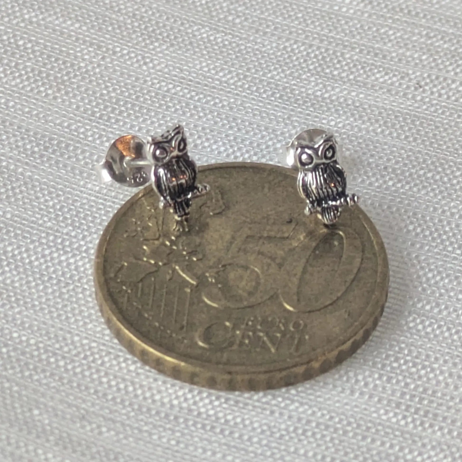 Paar detaillierte Eulen-Ohrstecker aus 925 Sterling Silber auf 50-Cent Münze fotografiert.