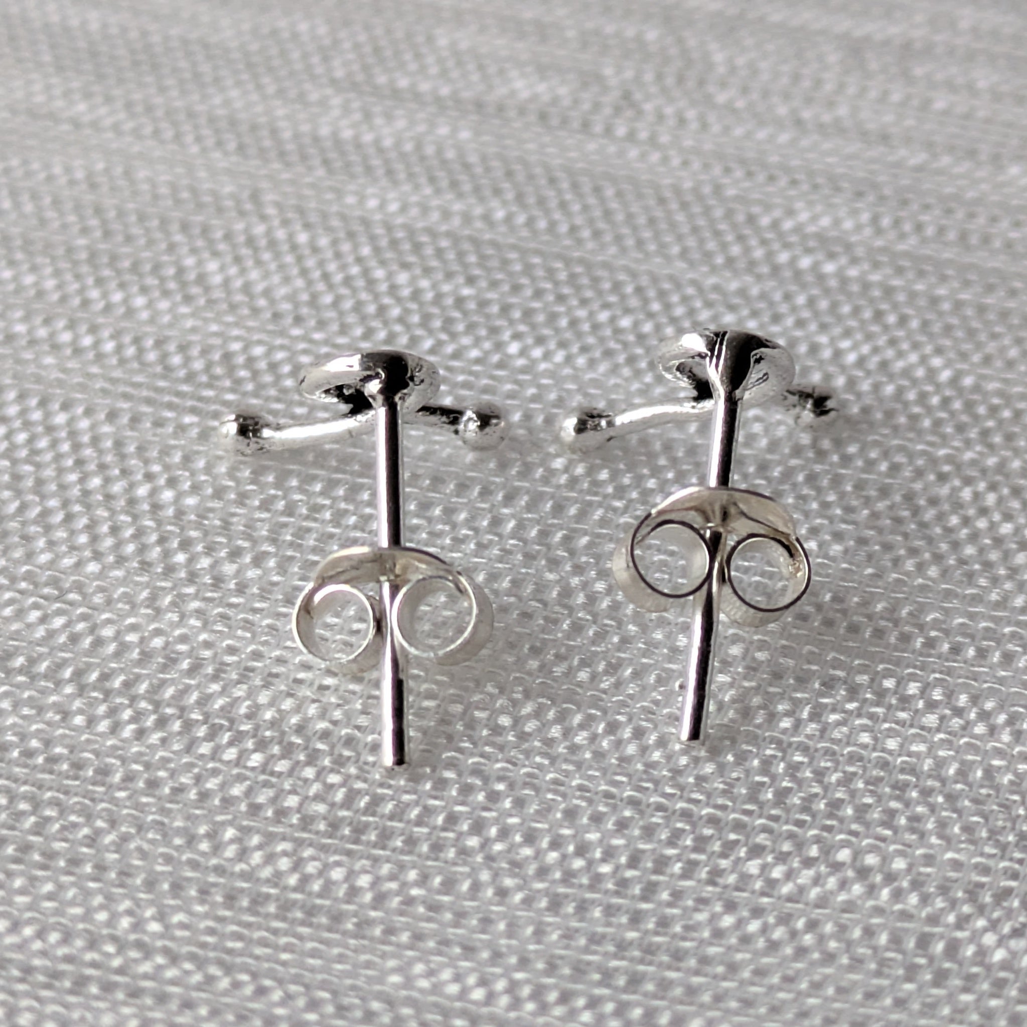 Paar silberner Schleifen-Ohrstecker mit polierter Oberfläche, fotografiert auf Textil