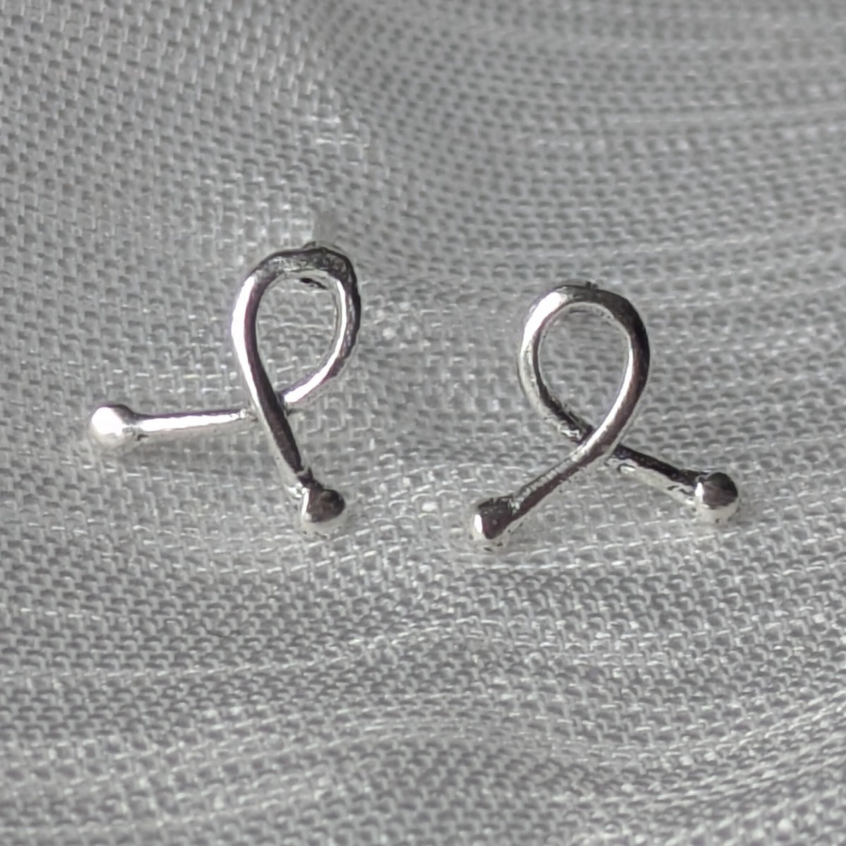 Mini-Ribbon Ohrstecker aus 925er Silber auf hellem Stoffhintergrund