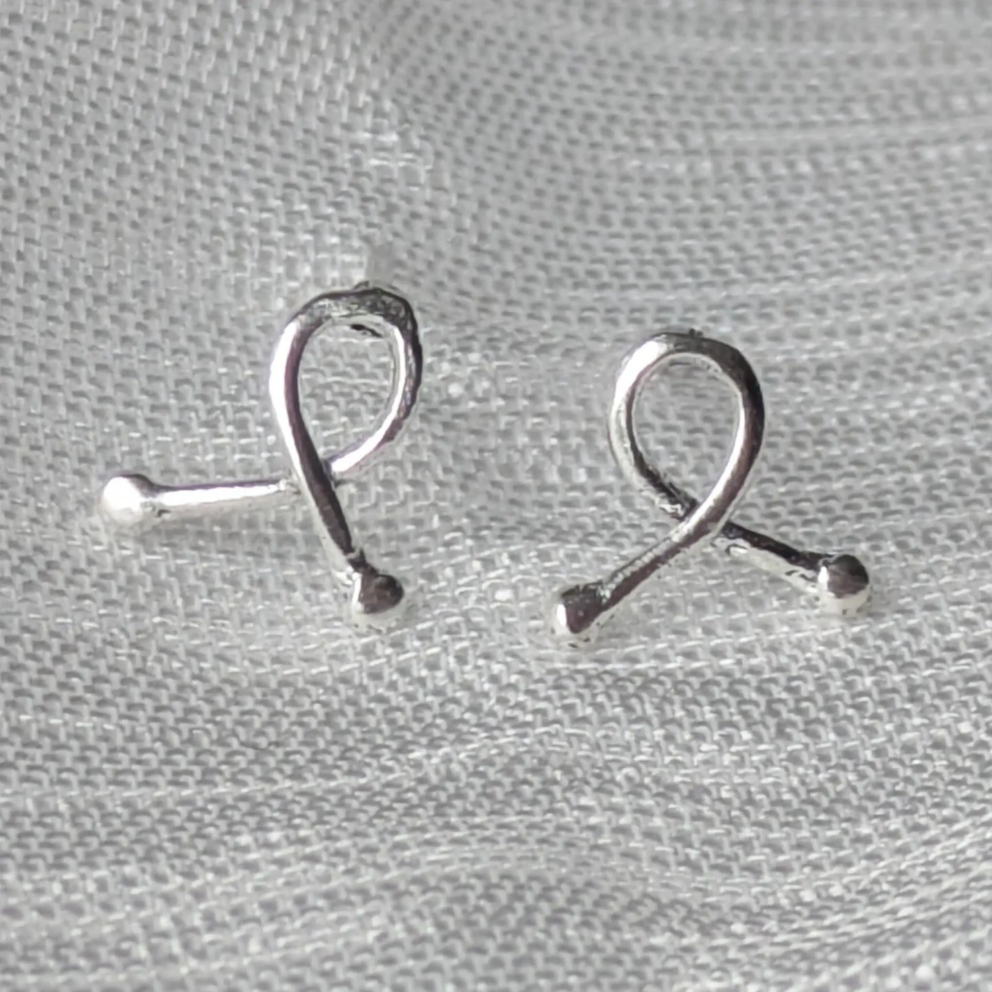 Mini-Ribbon Ohrstecker aus 925er Silber auf hellem Stoffhintergrund