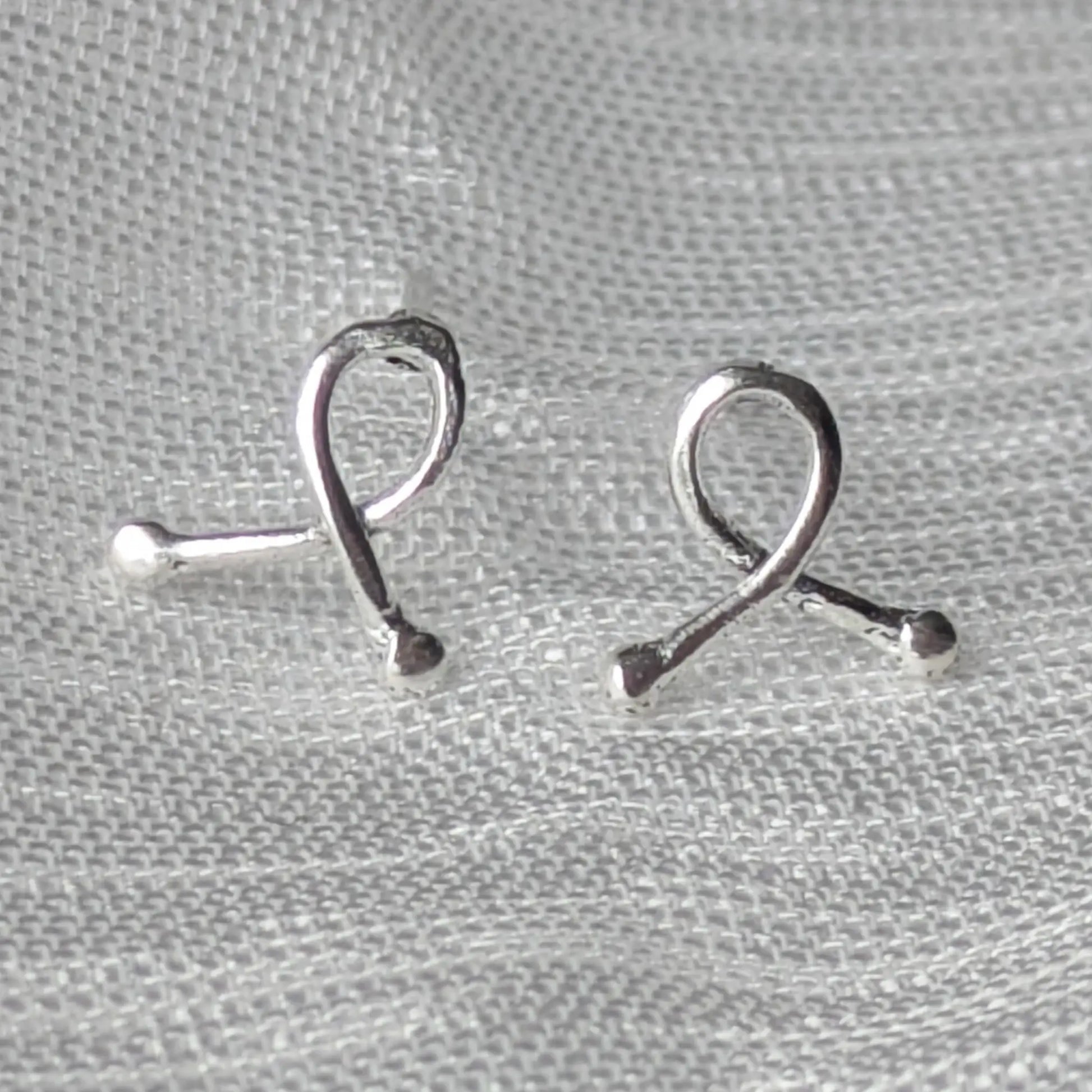 Mini-Ribbon Ohrstecker aus 925er Silber auf hellem Stoffhintergrund