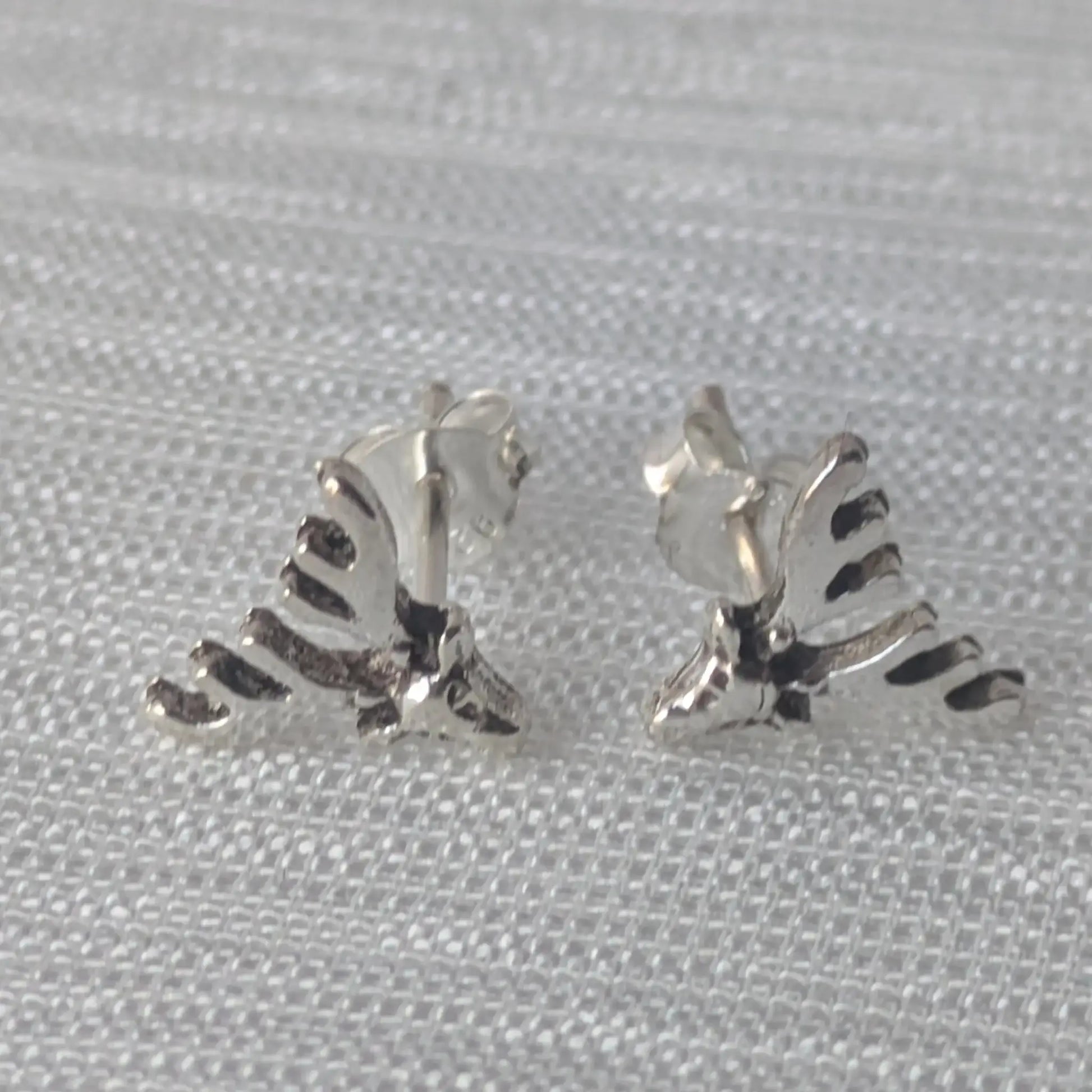 Zwei detaillierte Elch-Geweih-Ohrstecker aus glänzendem 925 Sterling Silber, liegend auf einem hellen, strukturierten Stoff.