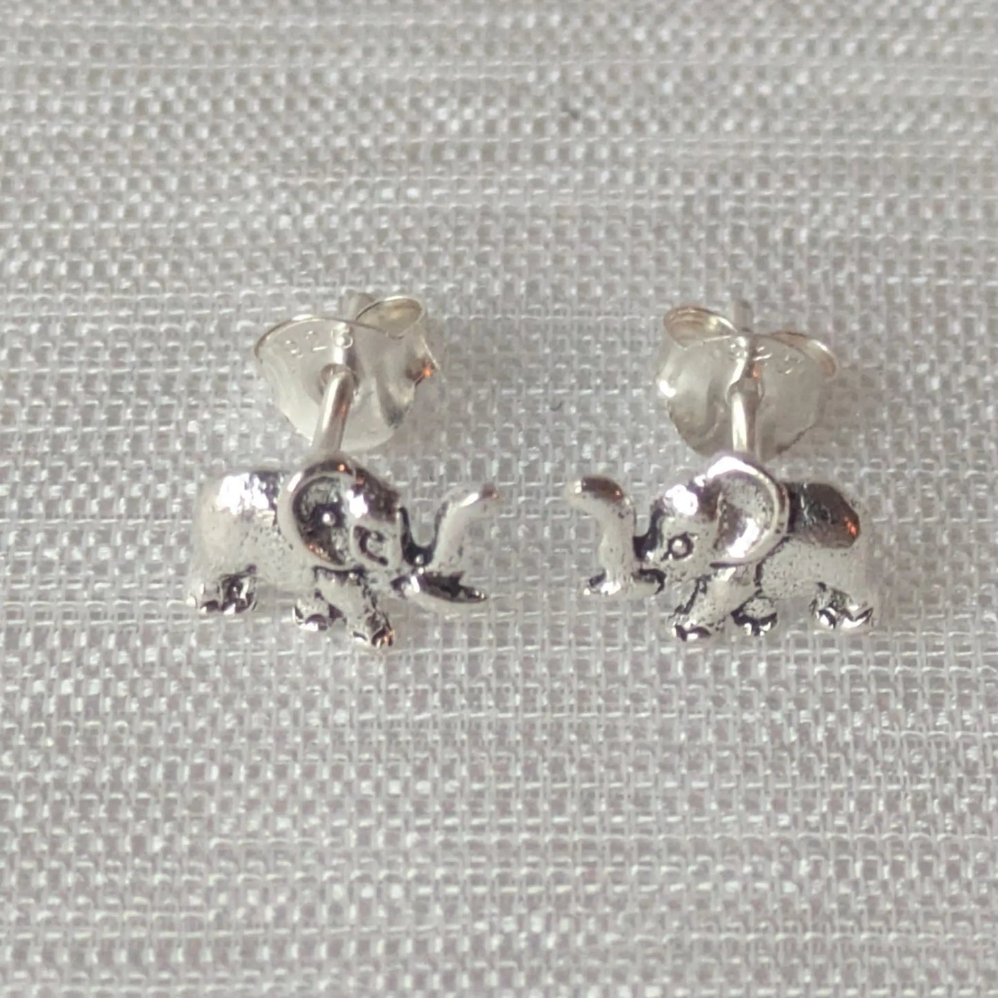 Zwei detaillierte Elefanten-Ohrstecker aus glänzendem 925 Sterling Silber auf einem hellen Stoffhintergrund.