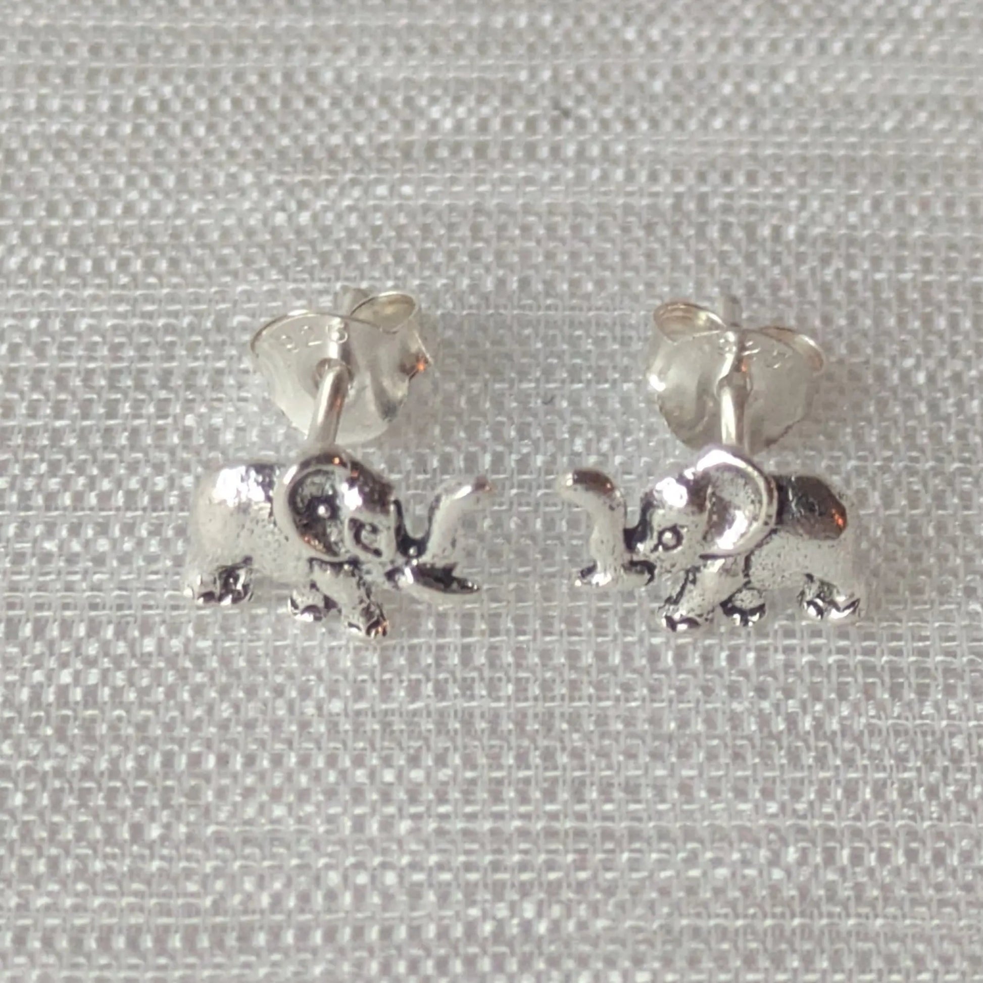 Zwei detaillierte Elefanten-Ohrstecker aus glänzendem 925 Sterling Silber auf einem hellen Stoffhintergrund.