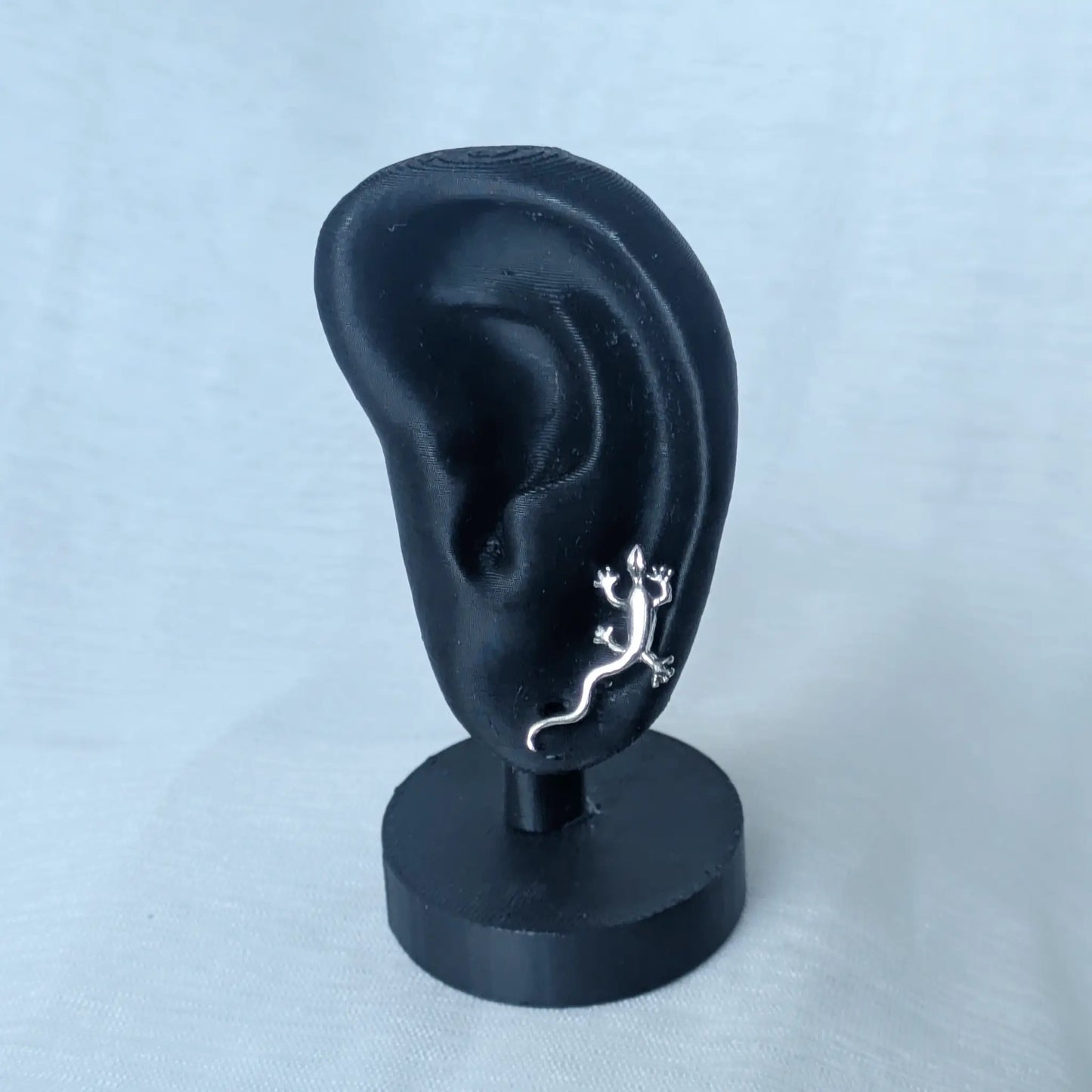 Ein realistisches schwarzes Ohr-Display, das den 925 Silber Gecko Ohrstecker getragen zeigt.