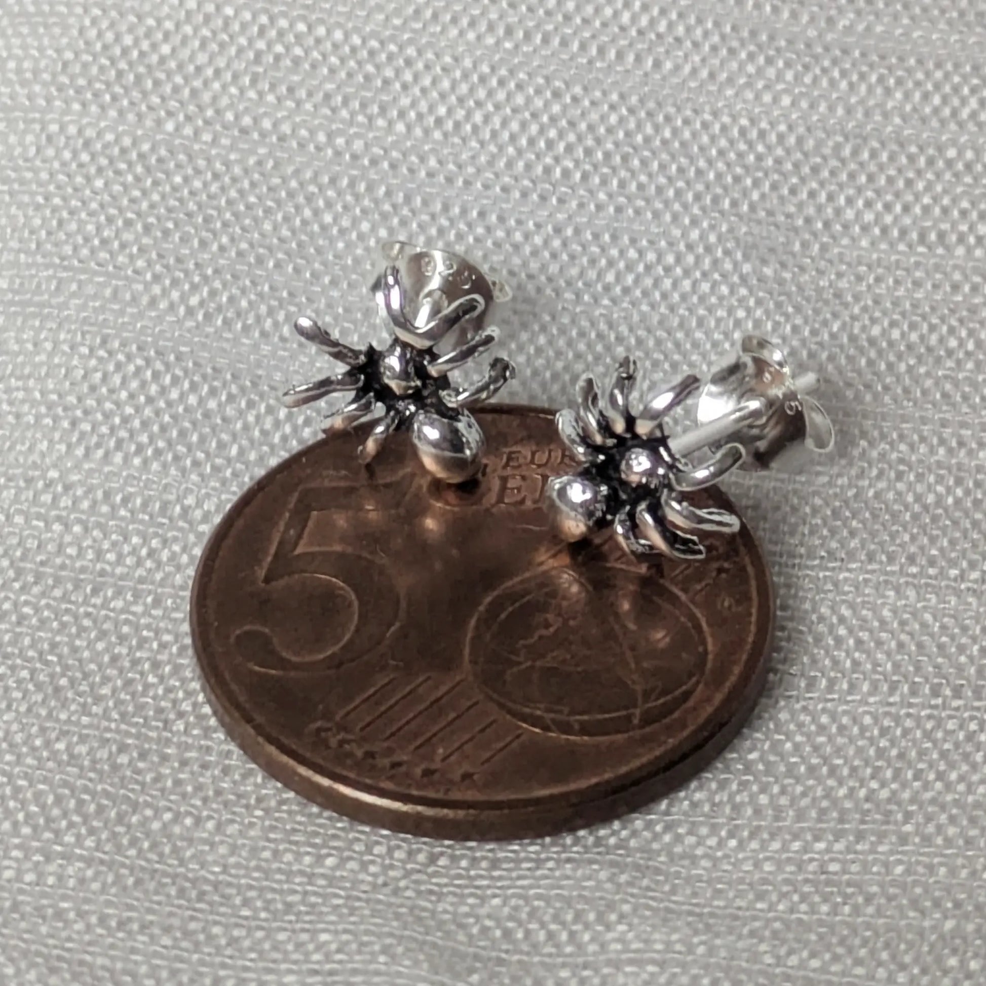 Größenvergleich der kleinen Spinnen-Silberohrringe auf einer 5-Cent-Münze zur Maßstäblichkeit.
