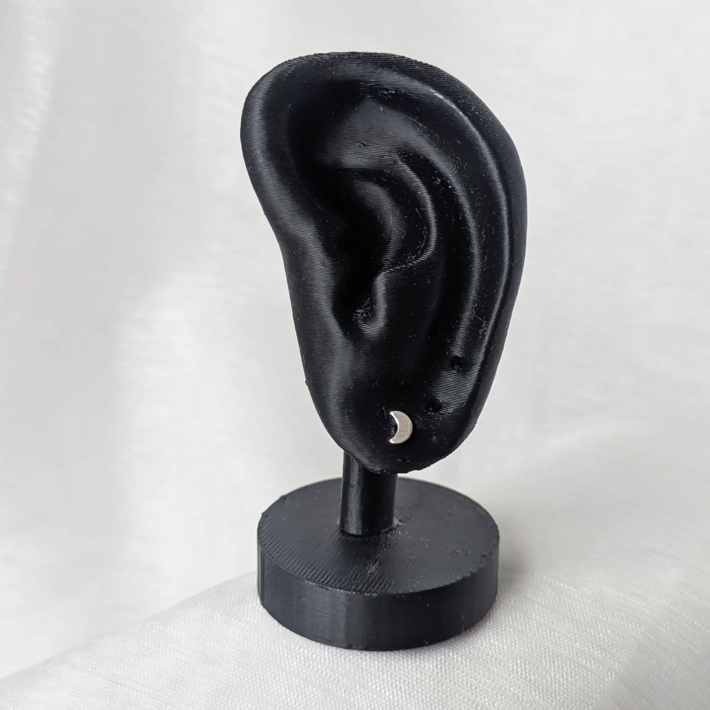 Mond-Ohrringe an schwarzem Display zur Demonstration der Passform am Ohr.