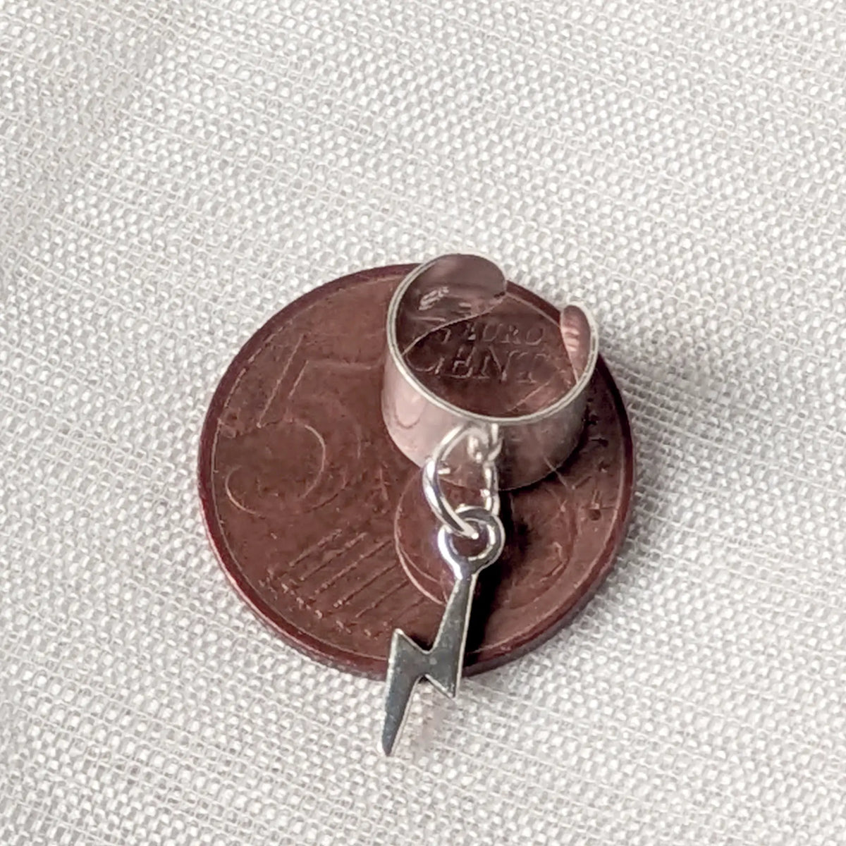 Silberner Earcuff mit Blitz-Anhänger liegend auf einer 5-Cent-Münze zum präzisen Größenvergleich.