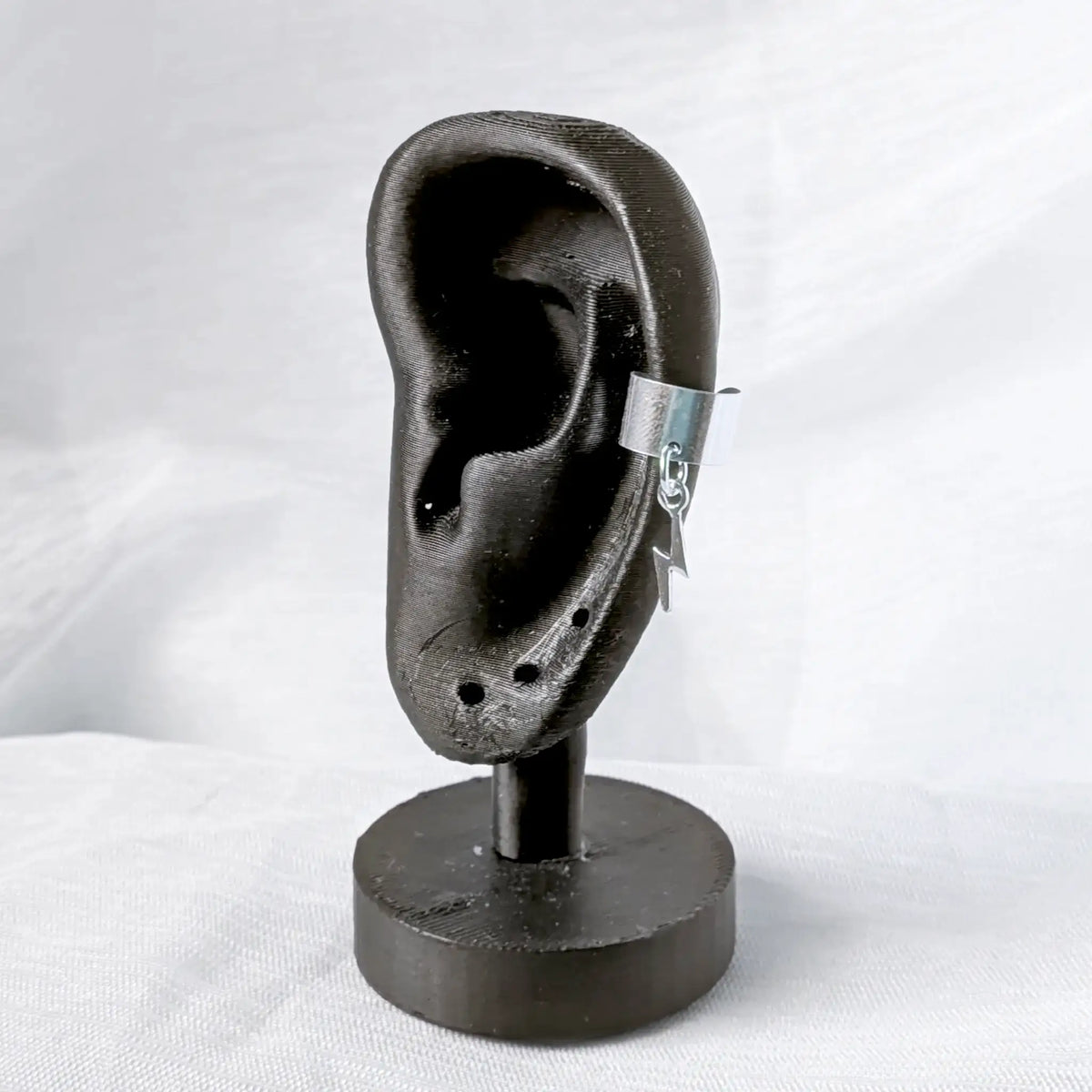 Rockiger Silber-Earcuff mit Blitz, sicher getragen am seitlichen Knorpel eines schwarzen Ohr-Displays.