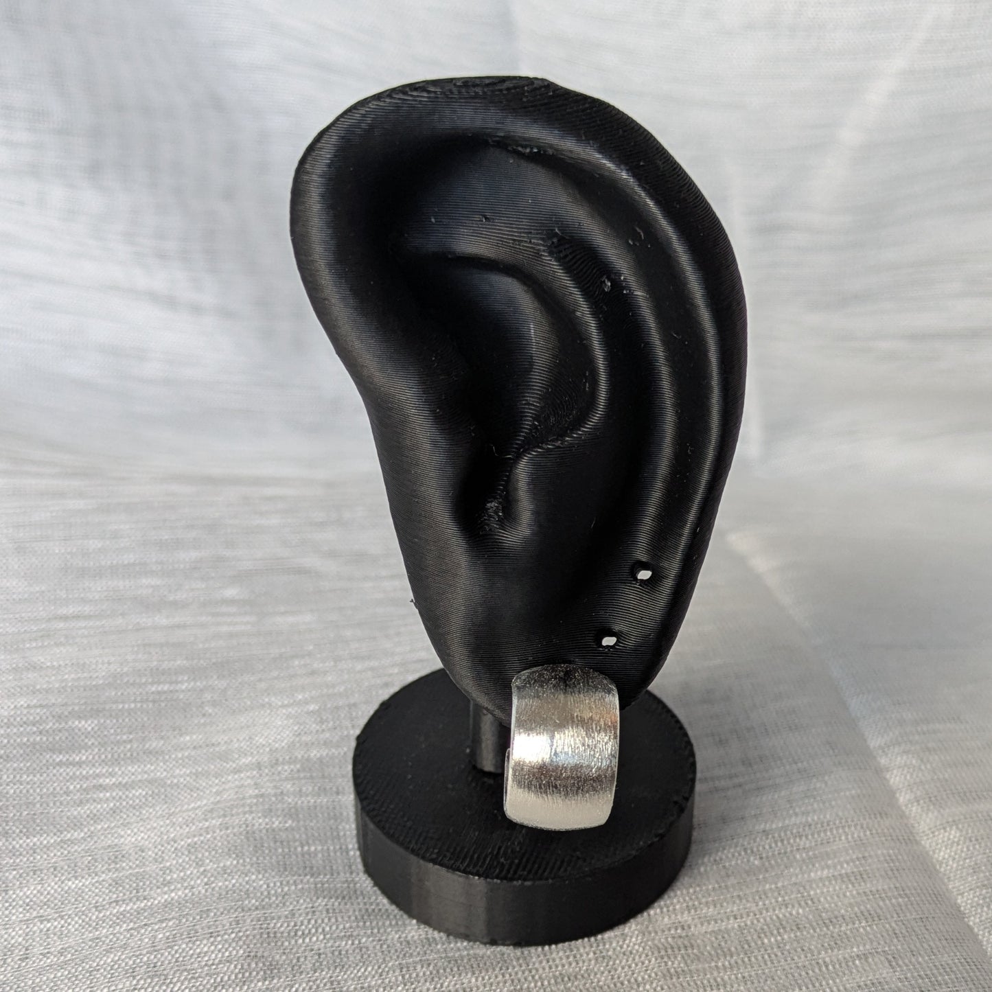 Gebürstete Silber‑Creolen mit Stecker und Butterflyverschluss an einerm schwarzen Ohr-Modell.
