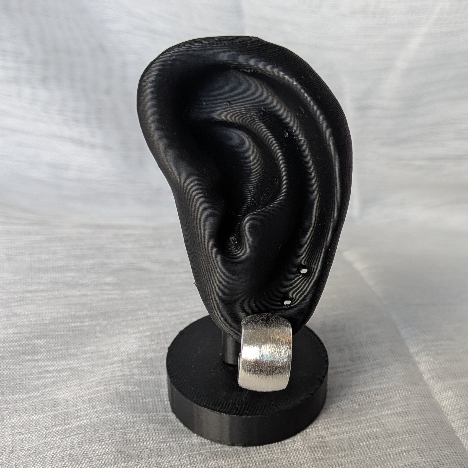 Gebürstete Silber‑Creolen mit Stecker und Butterflyverschluss an einerm schwarzen Ohr-Modell.
