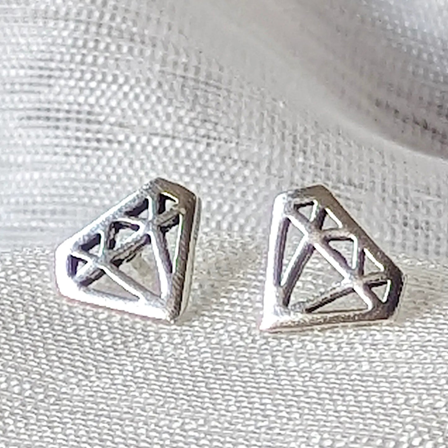 Detailreiche Nahaufnahme von zwei hochglanzpolierten Ohrsteckern in Diamanten-Form aus 925 Sterling Silber.