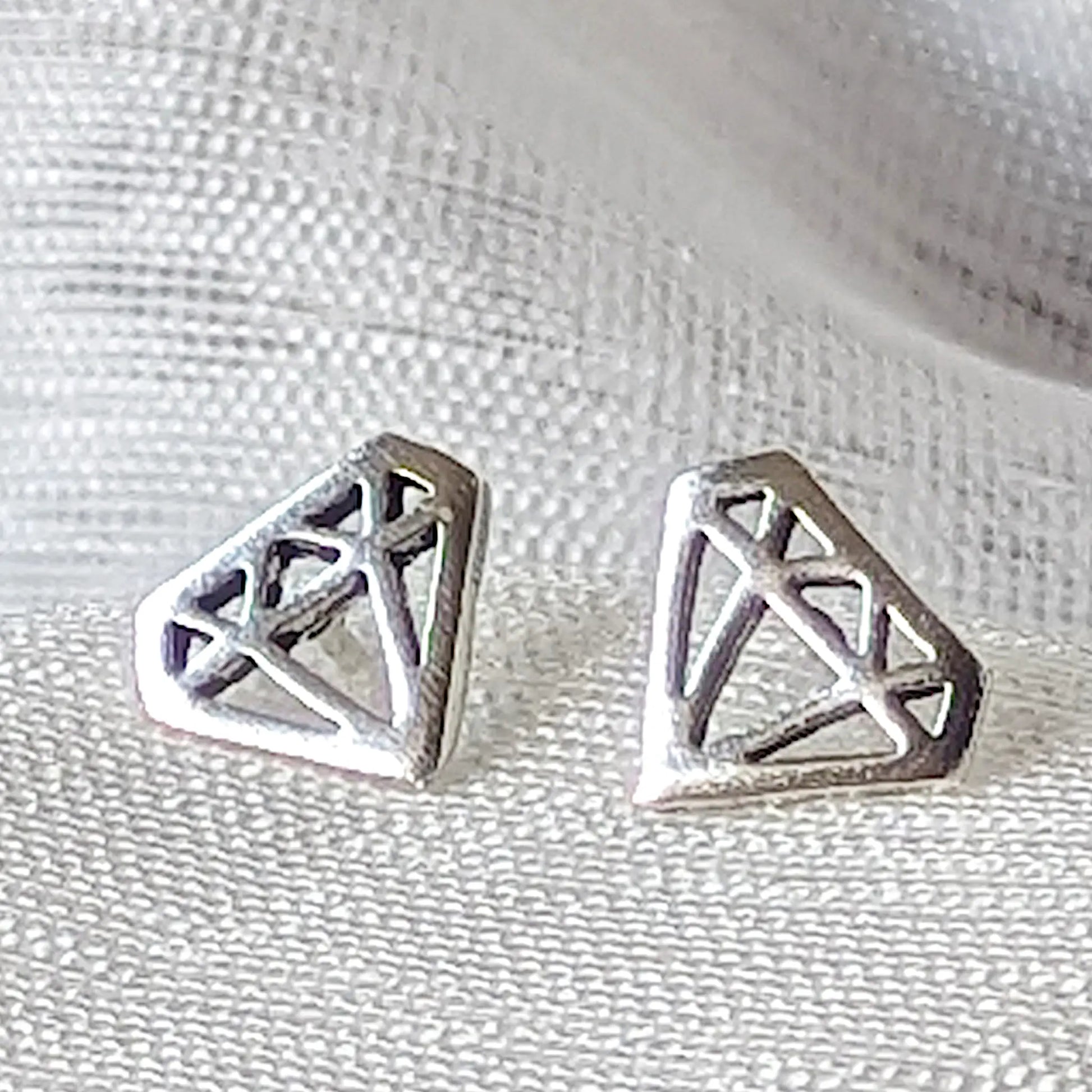 Detailreiche Nahaufnahme von zwei hochglanzpolierten Ohrsteckern in Diamanten-Form aus 925 Sterling Silber.