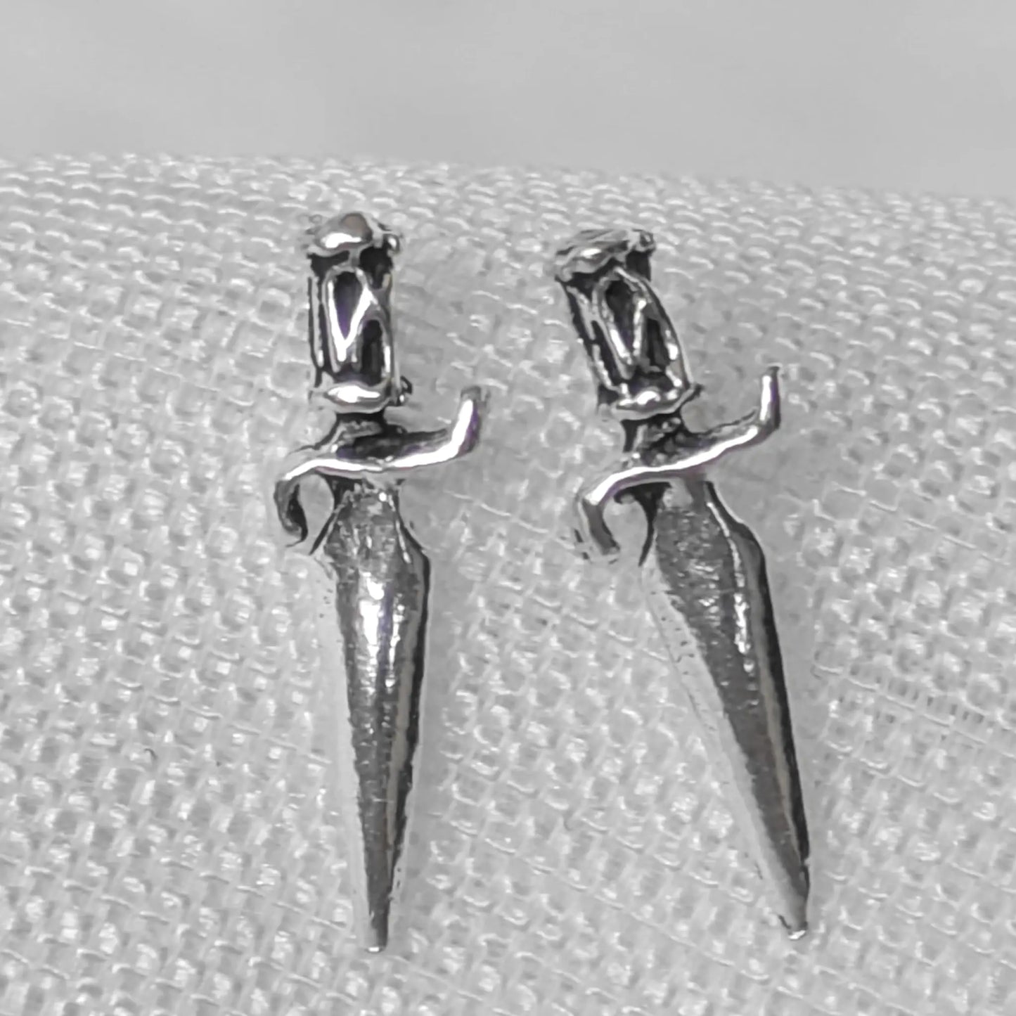 `Nahaufnahme von zwei filigranen Dolch-Ohrsteckern aus glänzendem 925 Sterling Silber mit detailliertem Griff.