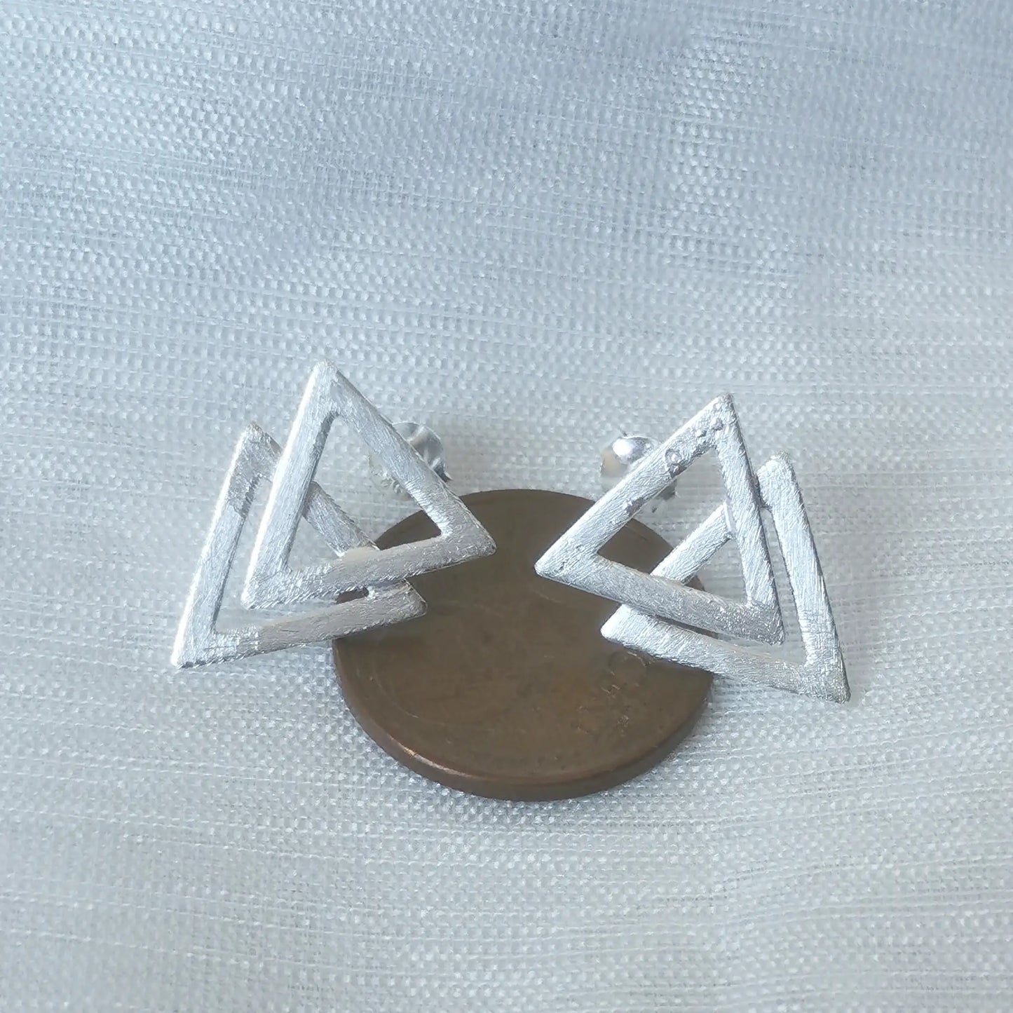 Größenvergleich: Die geometrischen Doppel-Dreieck-Silberohrringe platziert auf einer 5-Cent-Münze als visuelle Maß-Referenz.