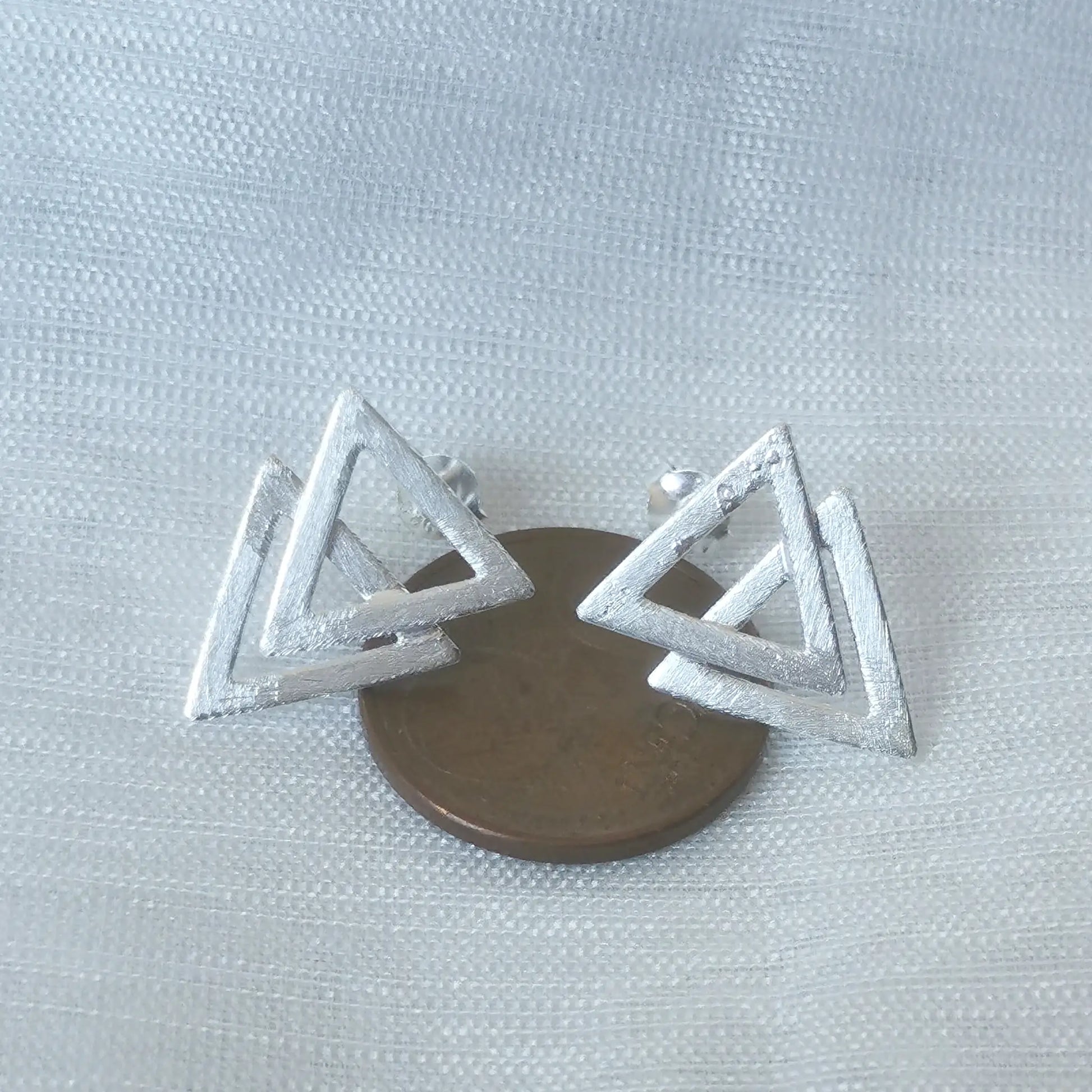 Größenvergleich: Die geometrischen Doppel-Dreieck-Silberohrringe platziert auf einer 5-Cent-Münze als visuelle Maß-Referenz.