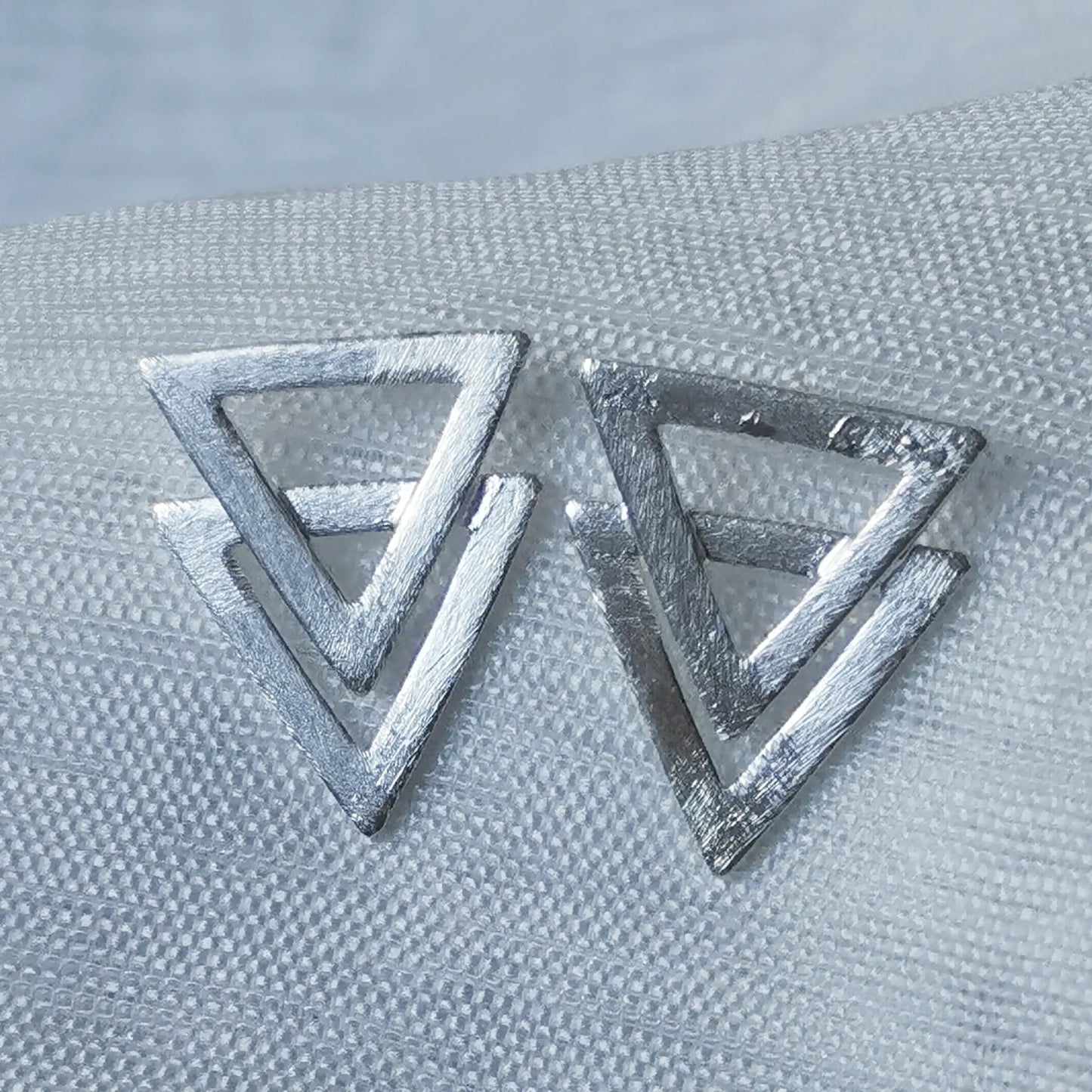 Nahaufnahme von zwei geometrischen 925 Silber Ohrsteckern im Doppel-Dreieck-Design mit mattierter, gebürsteter Oberfläche.