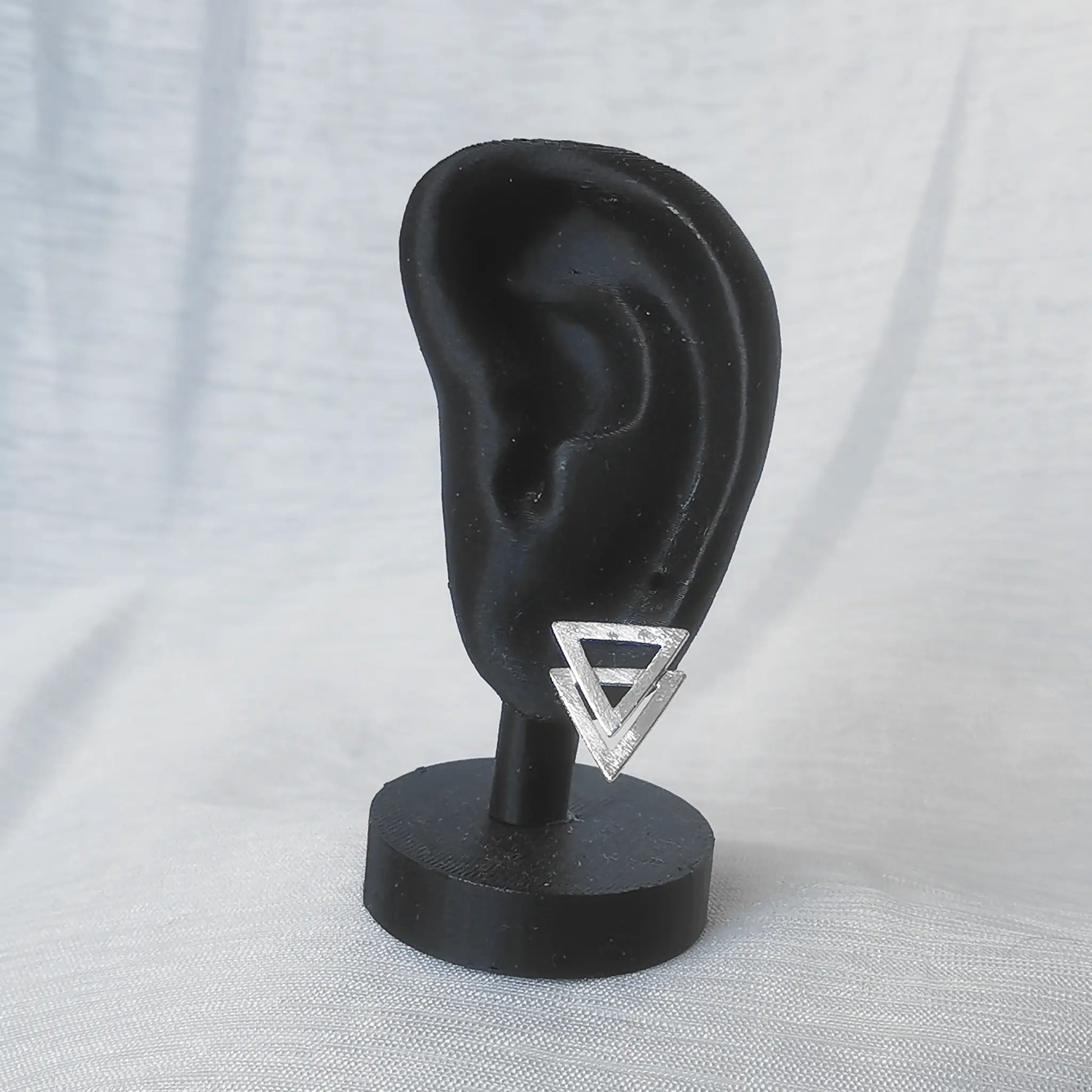 Ein mattierter 925 Silber Ohrstecker in doppelter Dreiecksform präsentiert an einem schwarzen Ohr-Display zur Veranschaulichung von Proportion und Größe.
