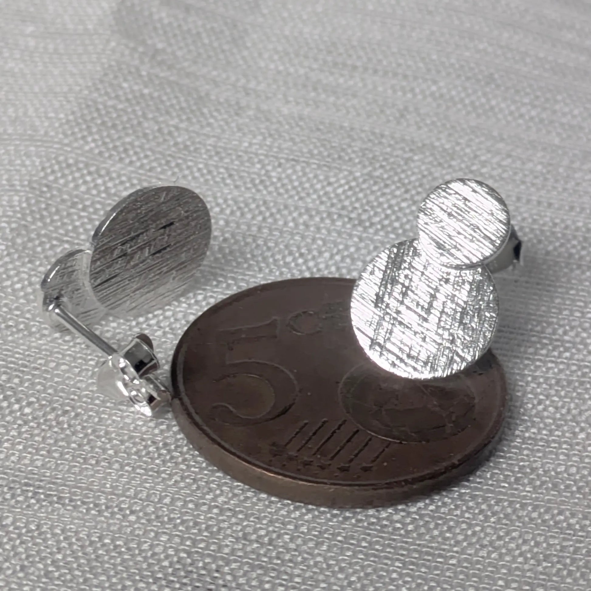 Größenvergleich der silbernen Ohrstecker auf einer 5-Cent-Münze.