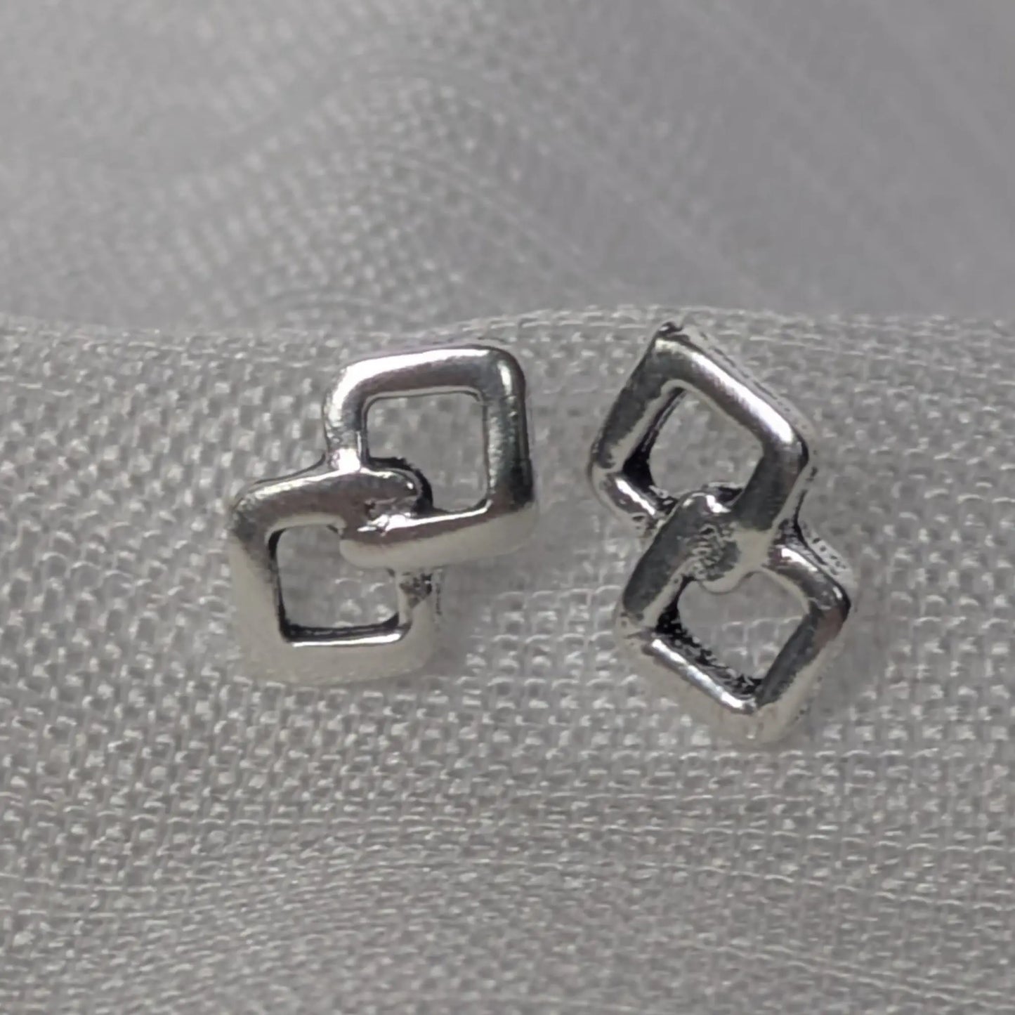 Silberne Ohrstecker mit zwei verschlungenen Rauten in der Frontalansicht auf weißem Stoff.
