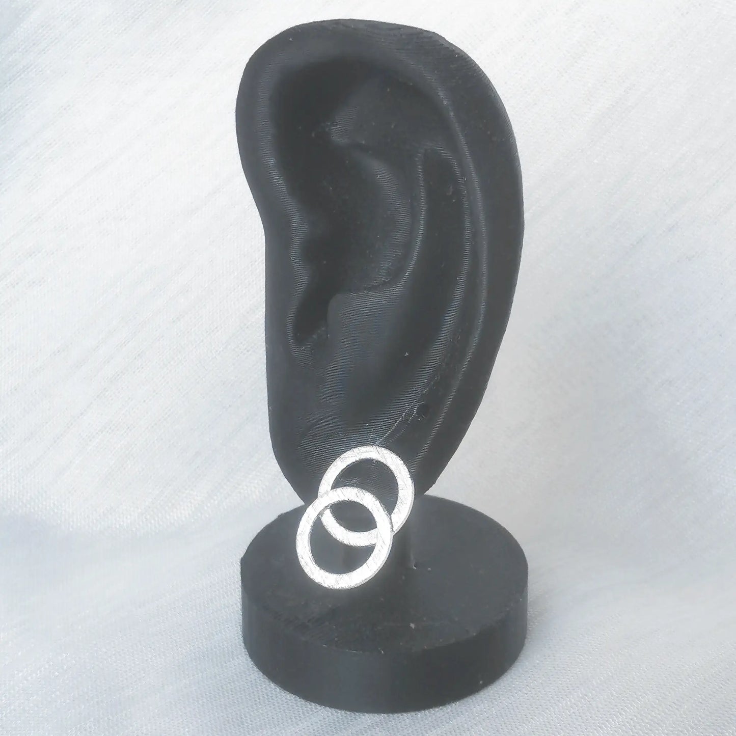 Die gebürsteten Silber-Ohrstecker in Doppelkreis-Form präsentiert an einem schwarzen Ohr-Modell zur exakten Einschätzung der Trageoptik.