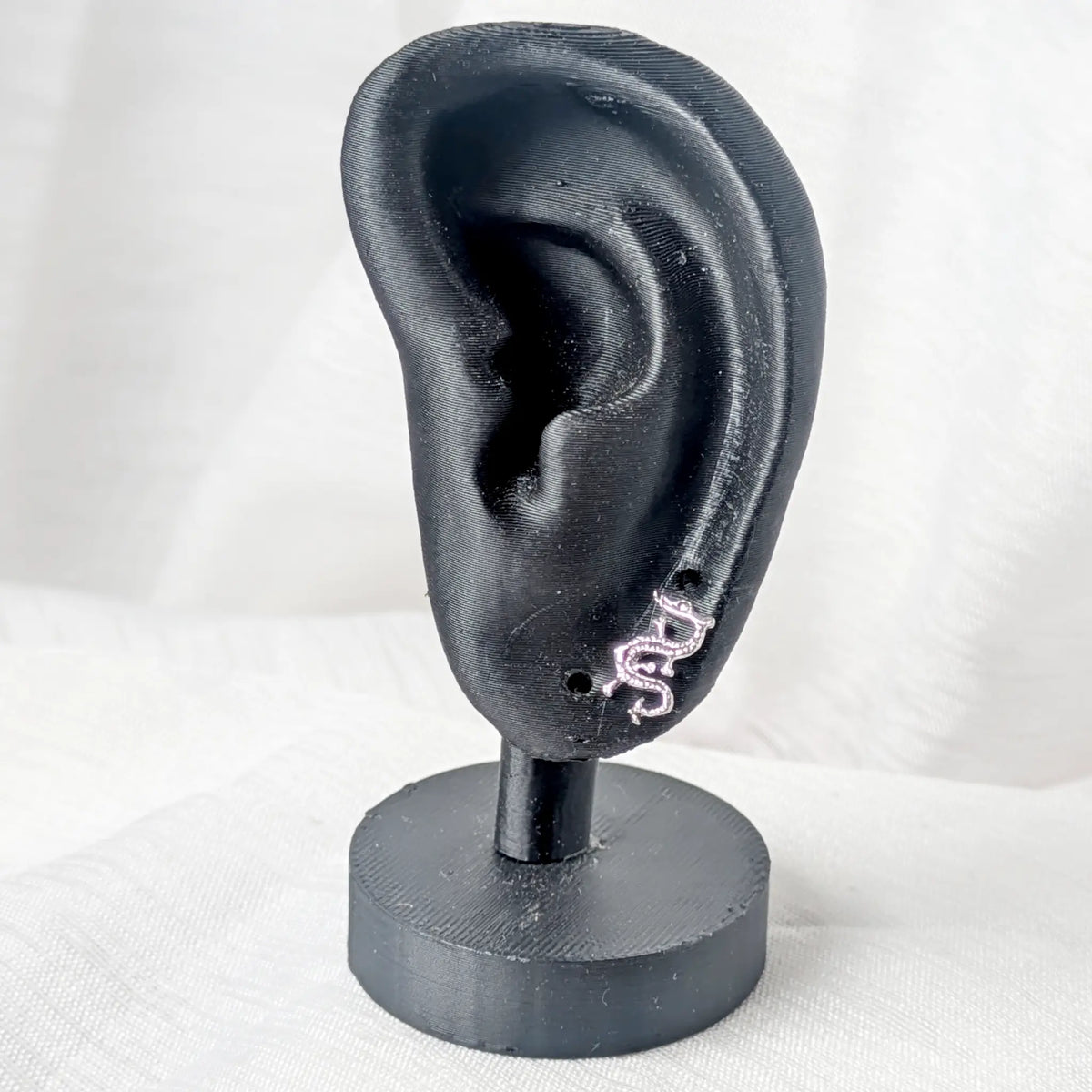 Ein kleiner silberner Drachen-Ohrstecker, getragen am Ohrläppchen eines schwarzen 3D-Modell-Ohrs.