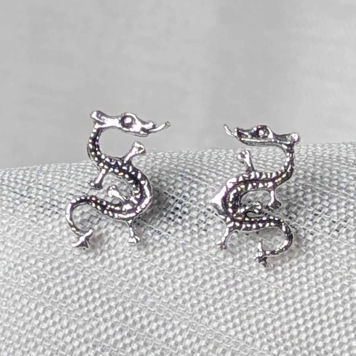 Nahaufnahme von zwei 925 Silber Ohrsteckern in Form asiatischer Drachen mit geschwärztem Schuppenmuster.
