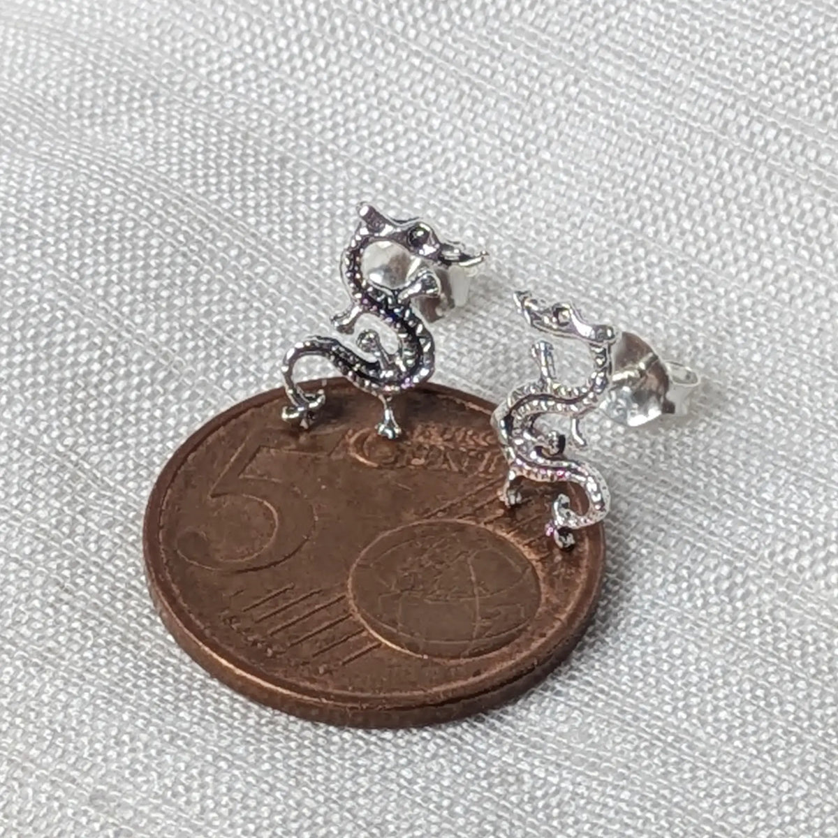 Silberner Drachen-Ohrstecker flach auf einer 5-Cent-Münze liegend für einen realistischen Größenvergleich im Alltag.