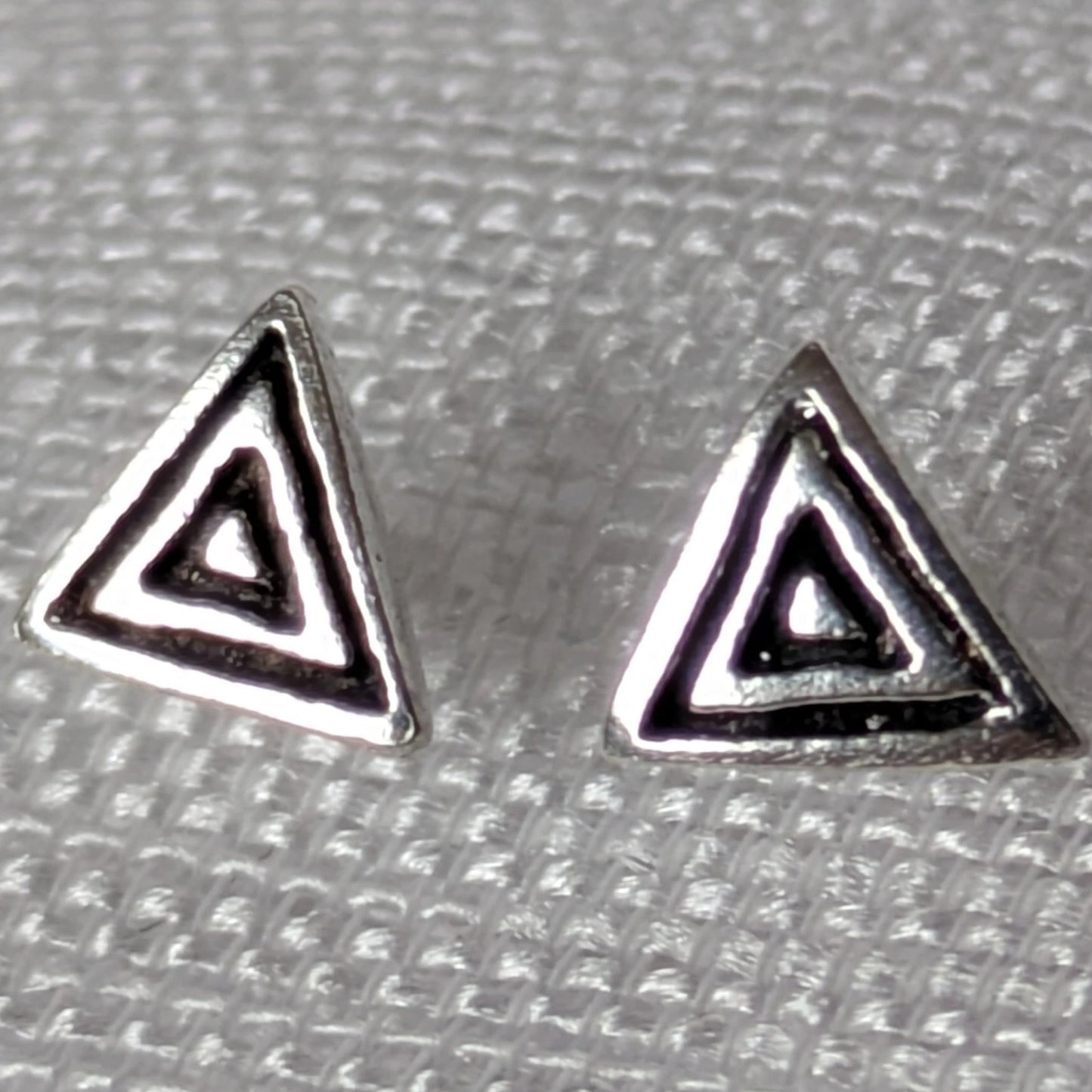 Frontalansicht der geometrischen Dreieck-Ohrstecker aus Silber mit dunklen Antik-Akzenten auf hellem Stoff.