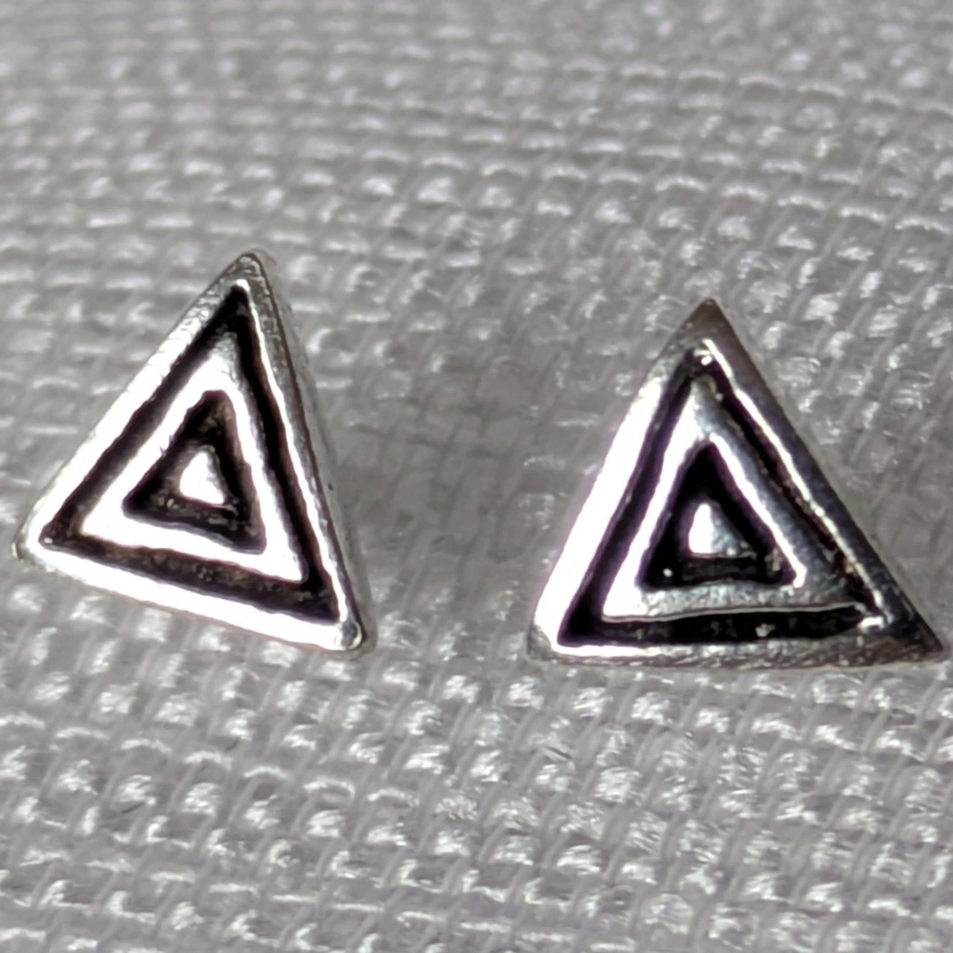 Frontalansicht der geometrischen Dreieck-Ohrstecker aus Silber mit dunklen Antik-Akzenten auf hellem Stoff.