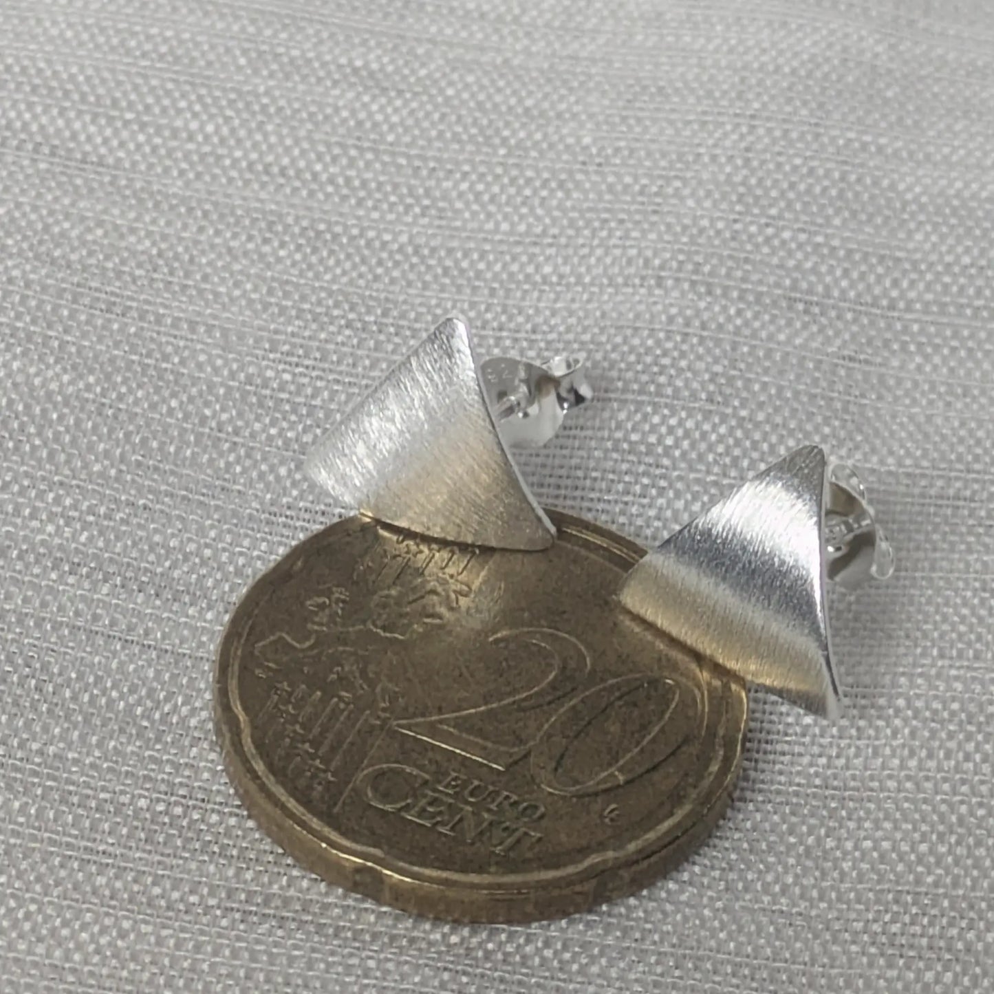 Größenvergleich der kleinen Dreieck-Ohrstecker auf einer 20-Cent-Münze.