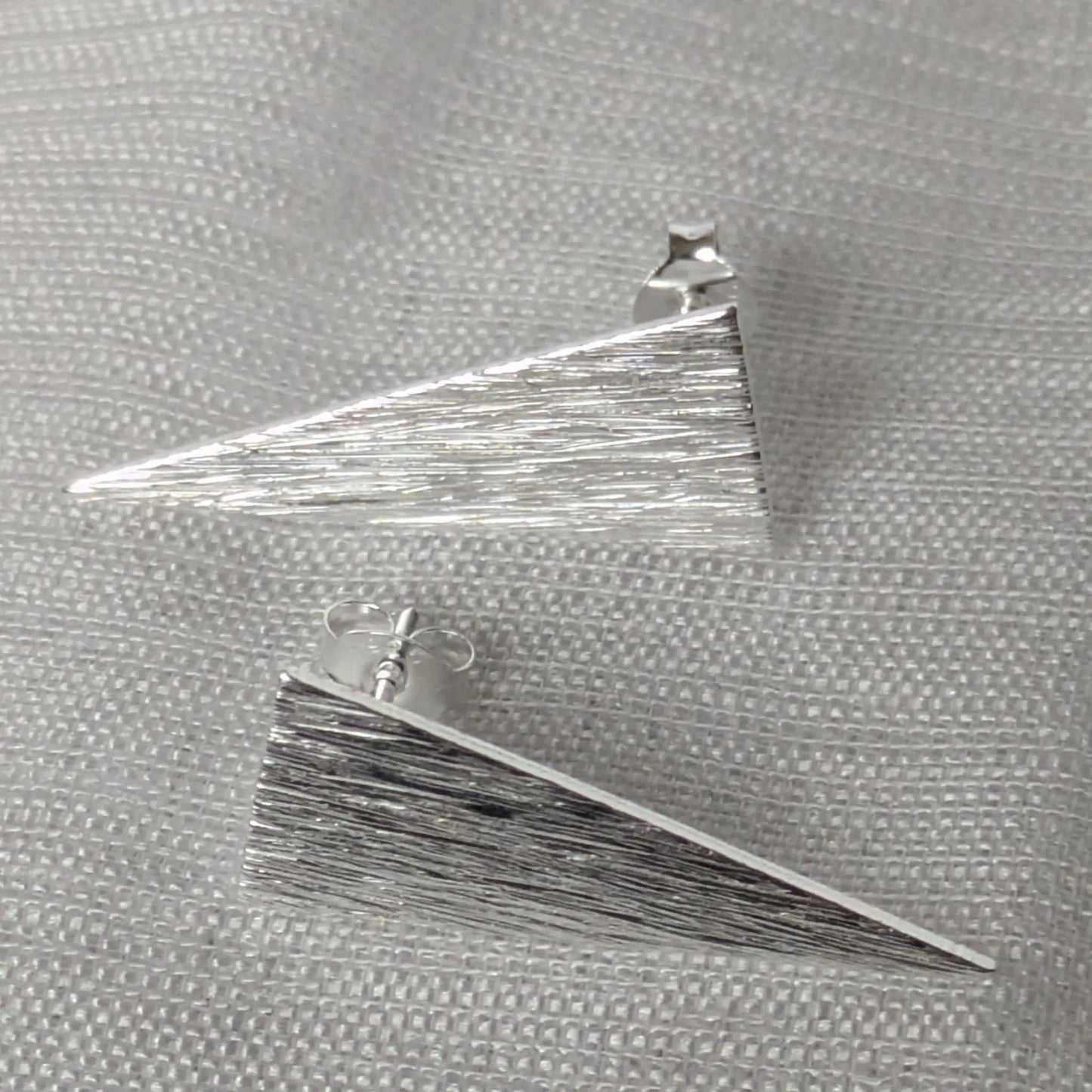 Paar geometrische Ohrringe aus Sterling Silber in Dreiecksform auf hellem Stoff.