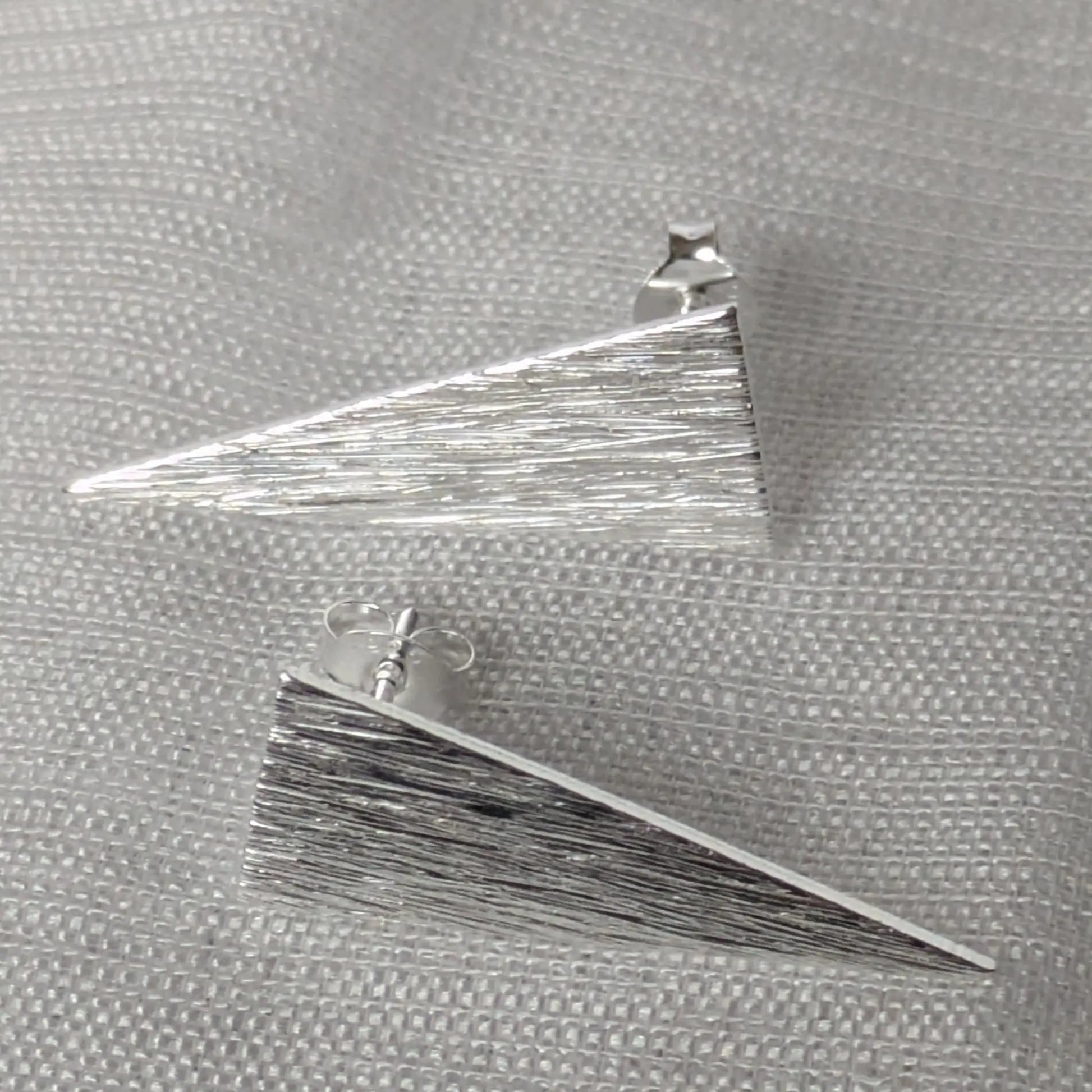 Paar geometrische Ohrringe aus Sterling Silber in Dreiecksform auf hellem Stoff.