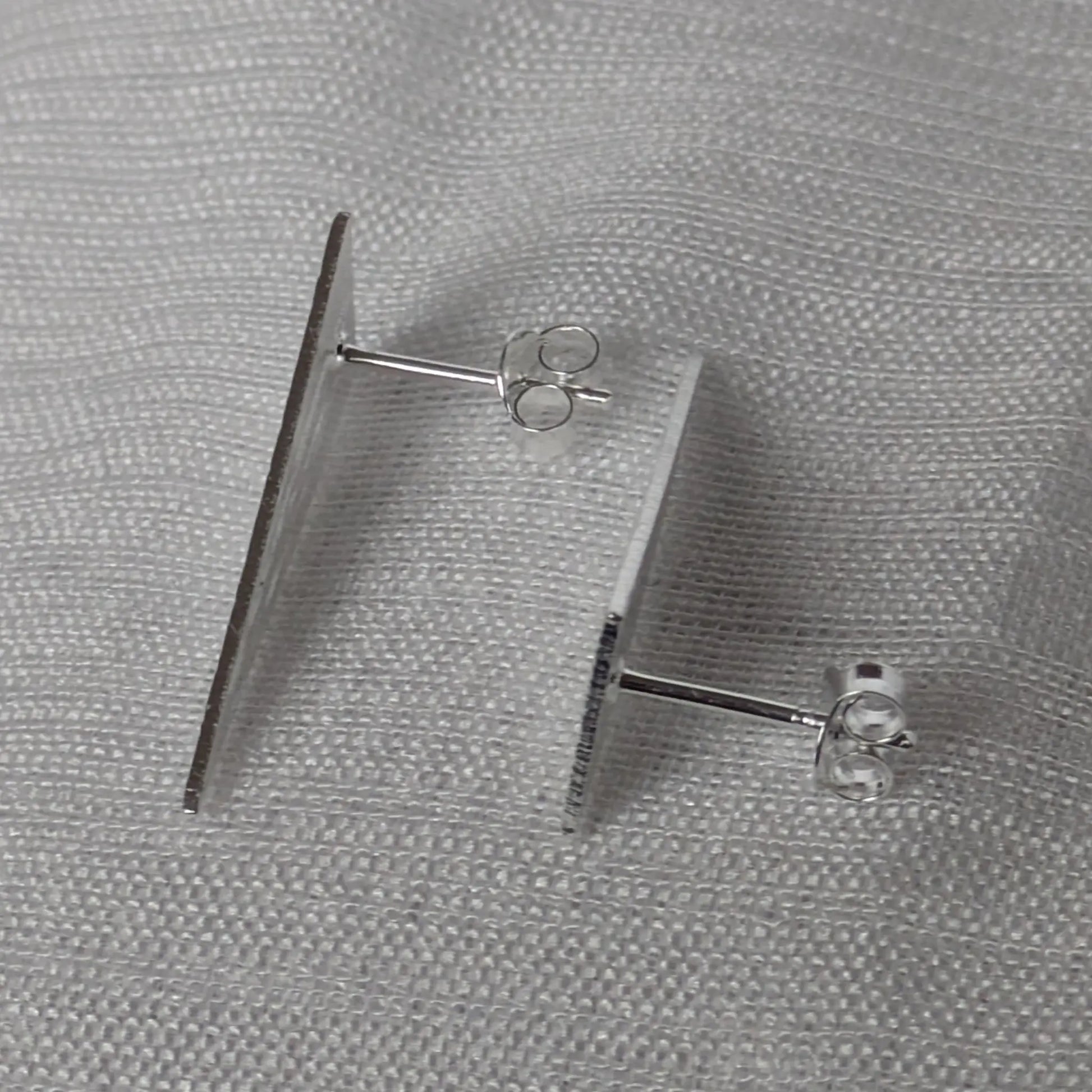 Seitenansicht der flachen silbernen Dreieck-Ohrstecker mit sicherem Verschluss.
