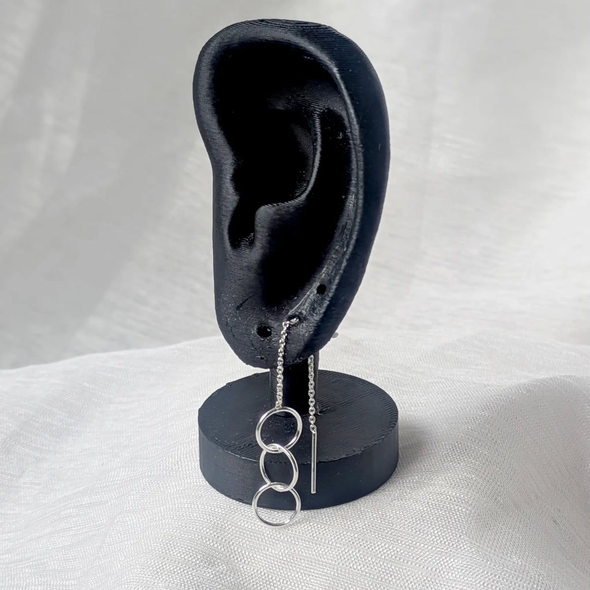 Silberner Durchzieher-Ohrring, getragen am Ohrloch eines schwarzen Modell-Ohrs, wobei Kette und Kreise auf der Vorderseite elegant herabfallen.