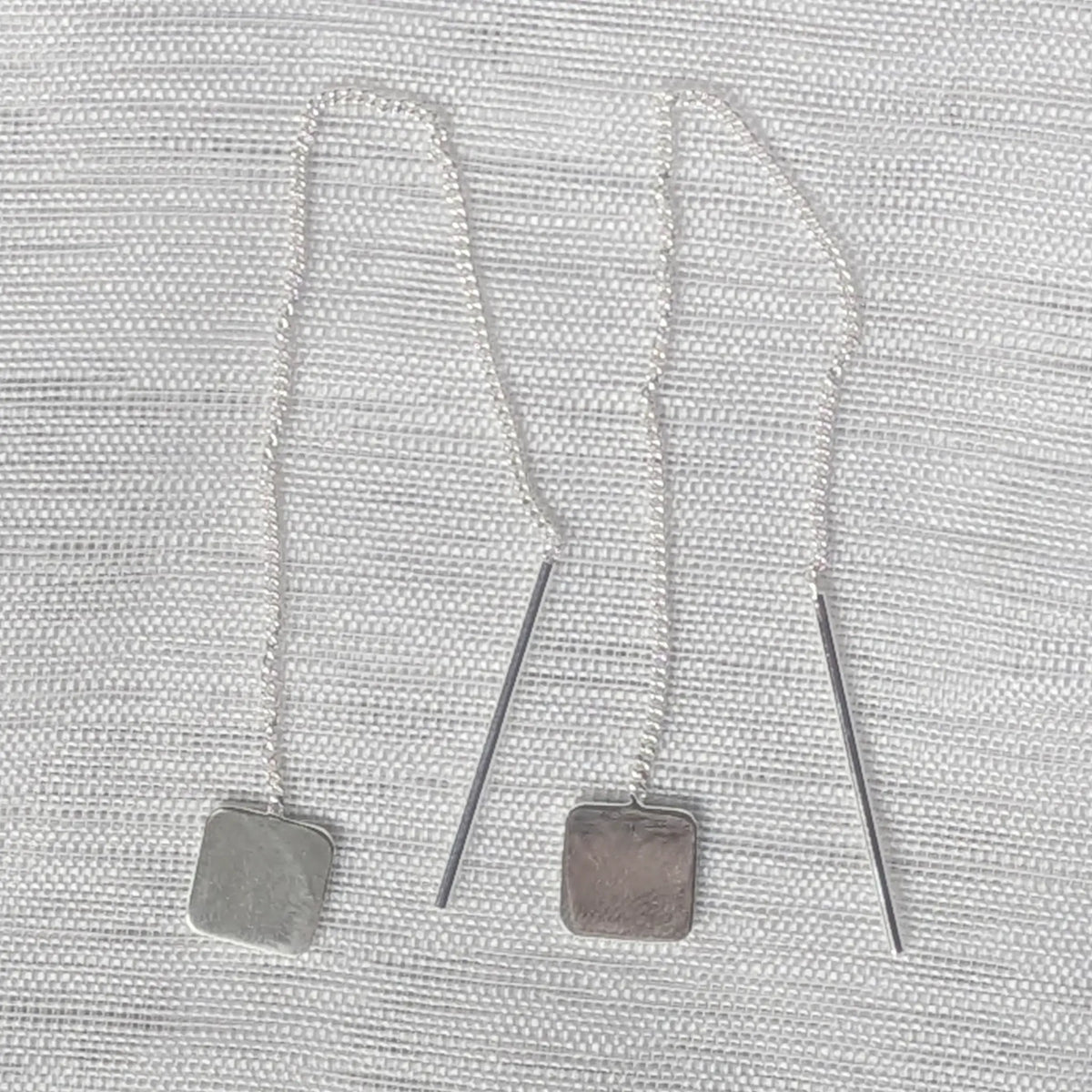 Frontalansicht der minimalistischen Kettenohrringe aus Silber, Fokus auf das geometrische Quadrat-Design am unteren Ende.